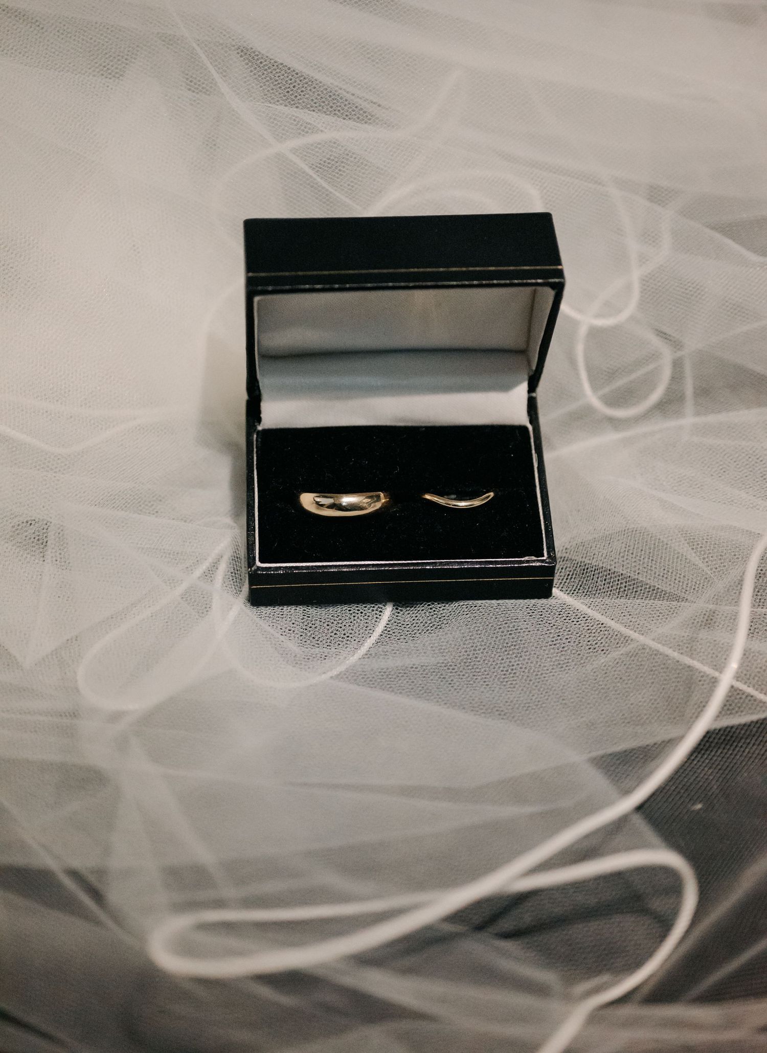 Wedding rings displayed in an elegant black box against a soft white tulle background.