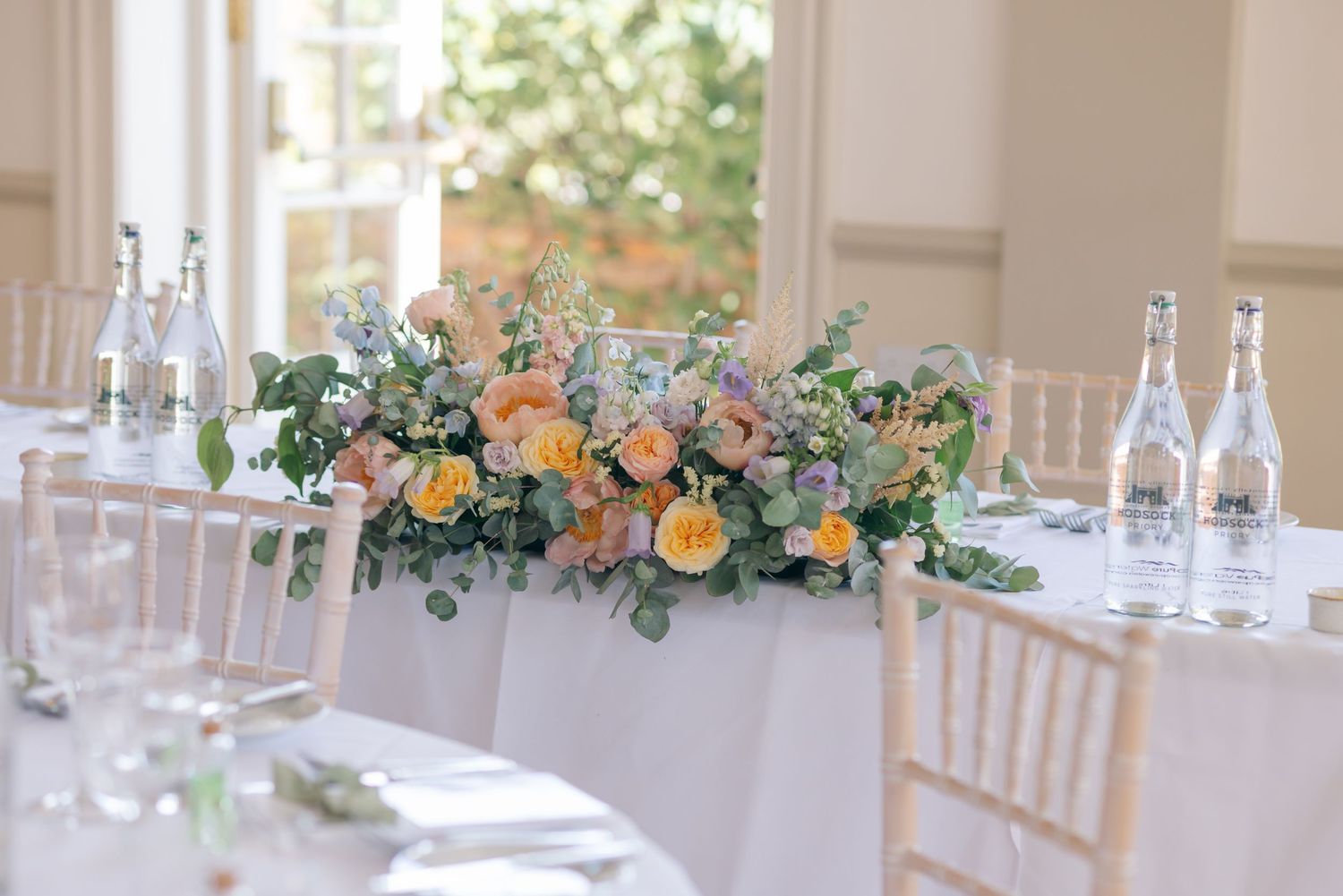 Elegant wedding reception table setting with floral centerpieces and white chiavari chairs.