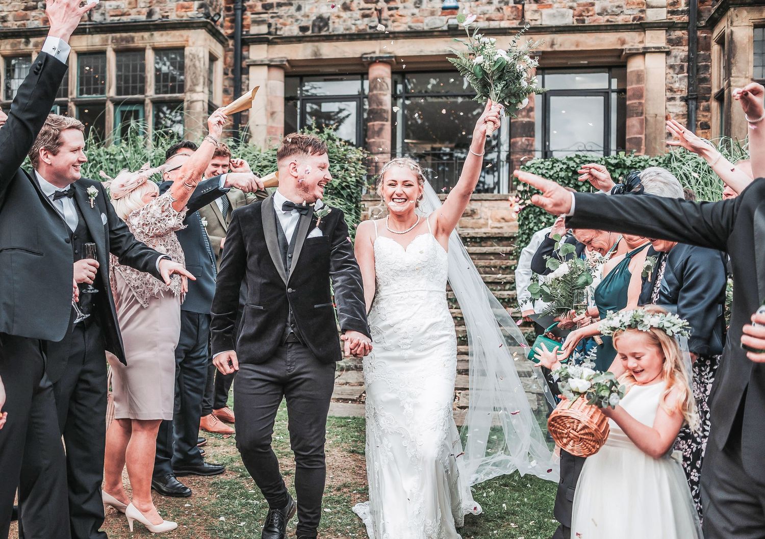Wedding guests throw pink rose petals in celebration during an outdoor ceremony at a rustic venue.