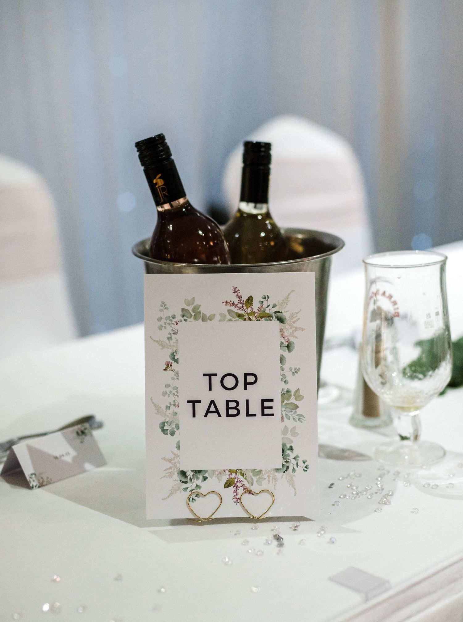 Elegant table number sign with floral design holds wine bottles at wedding reception.