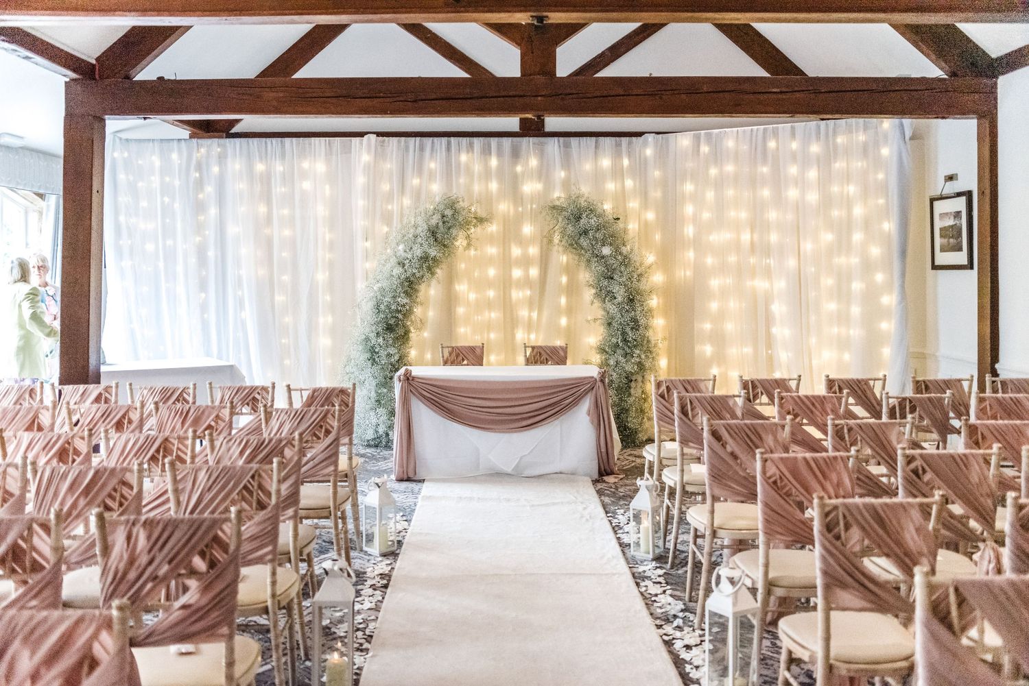 Elegant wedding ceremony setup with floral arch and wooden beams in an indoor venue.
