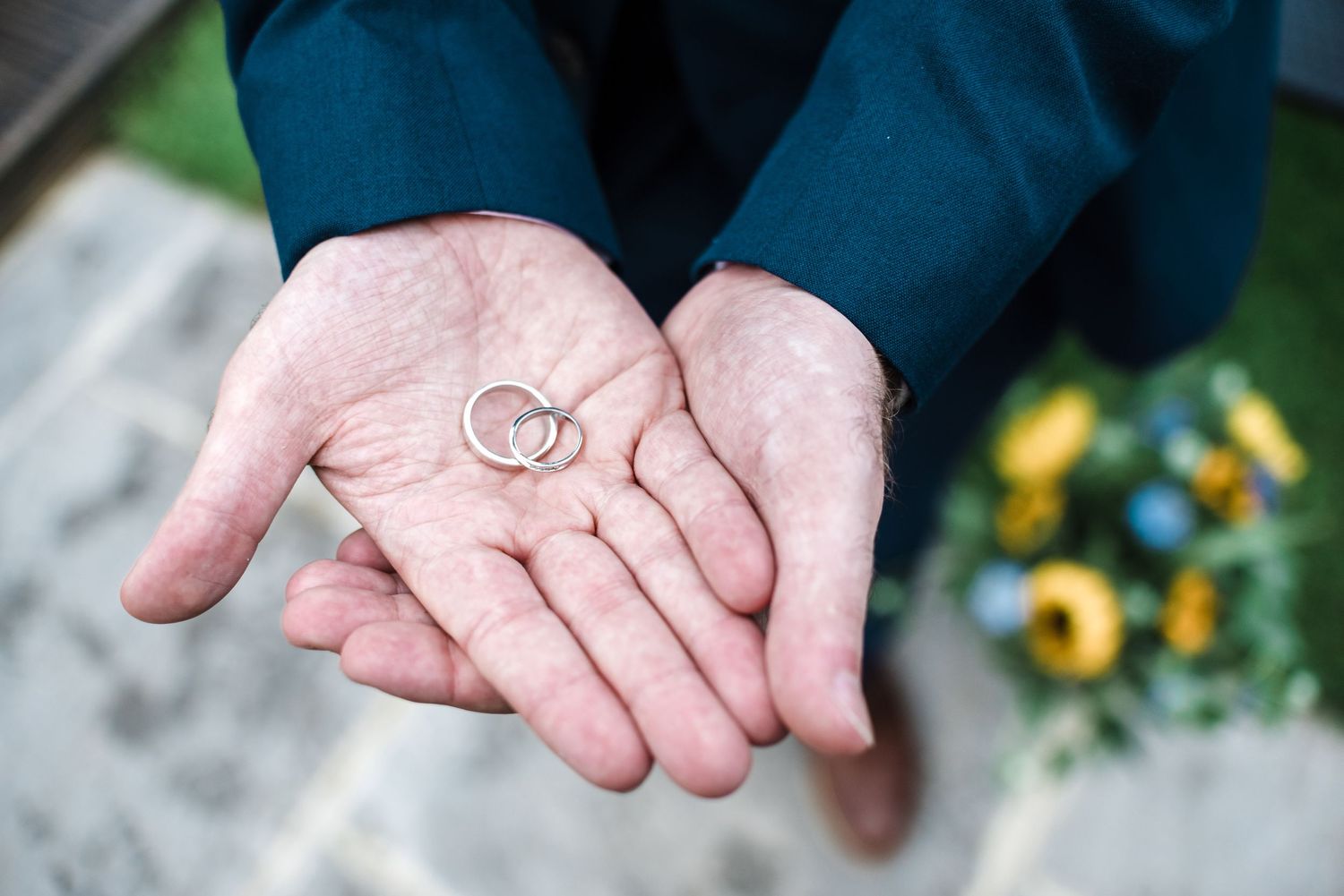 Wedding rings held delicately in open palms against a navy blue suit.