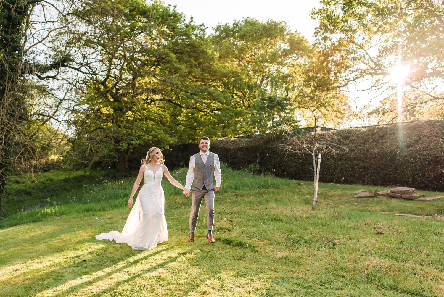 A couple walks hand in hand through a sunlit garden during golden hour.