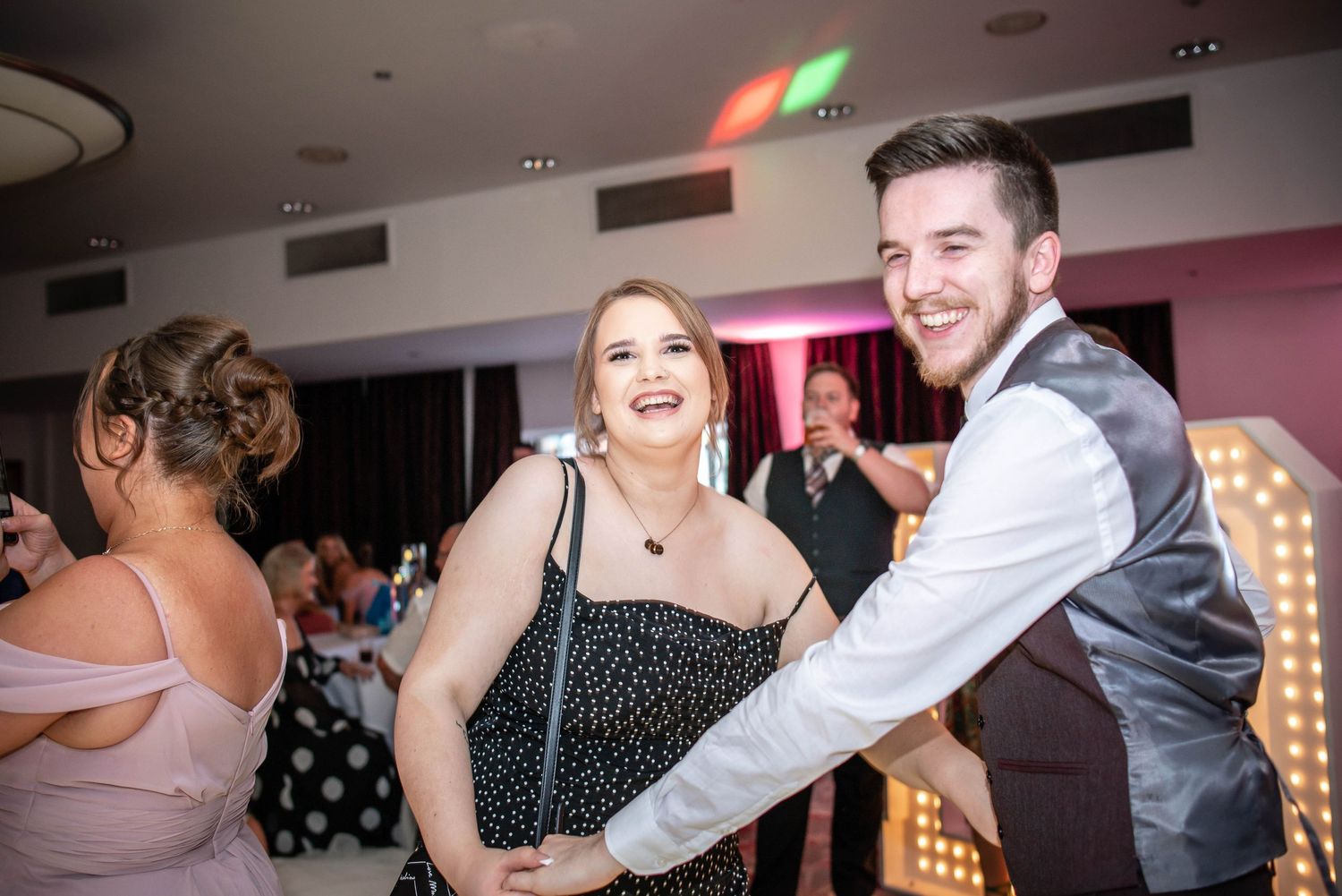 Wedding reception dance floor moment captured under colorful party lights.