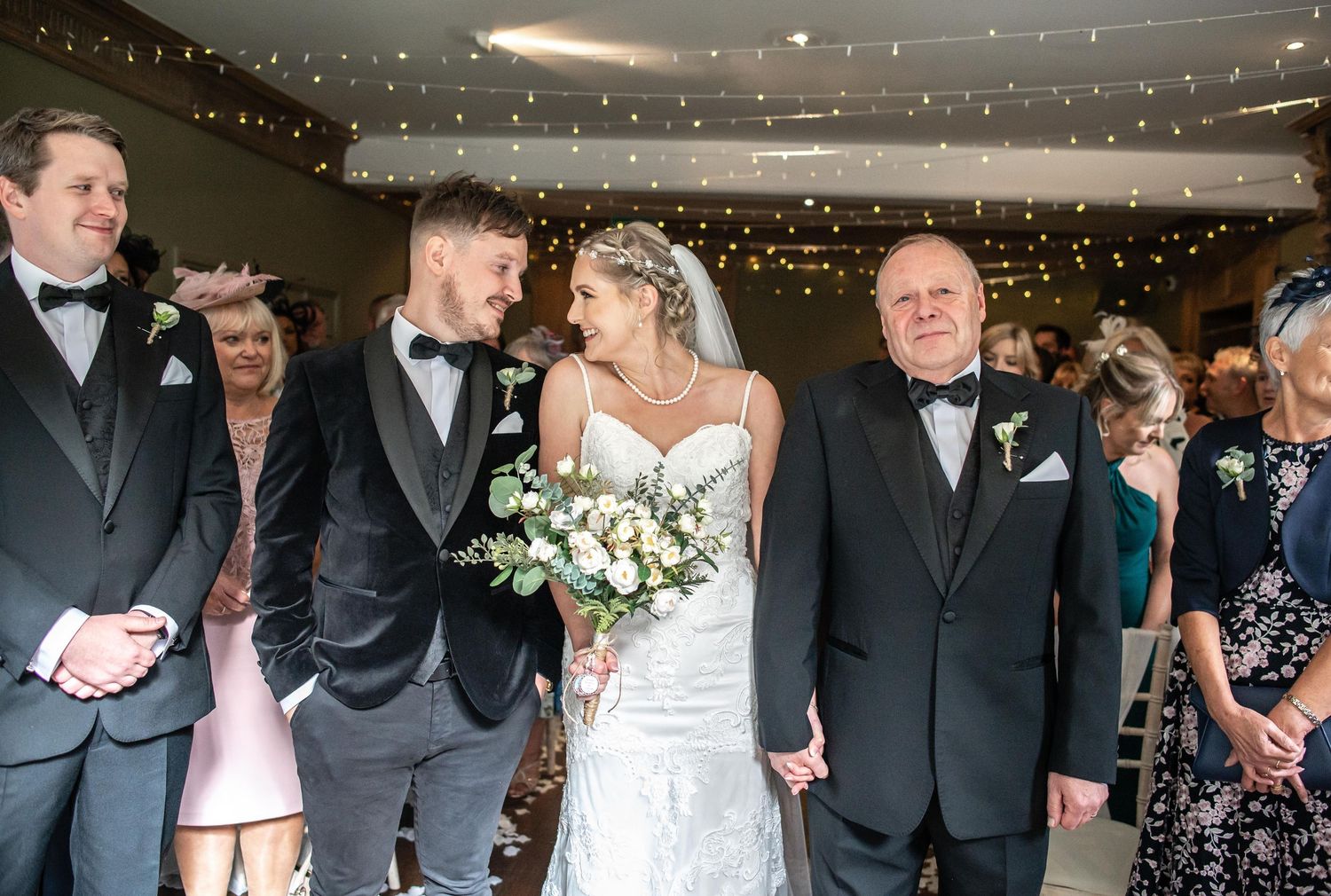 Wedding ceremony indoors with string lights decorating the ceiling and floral arrangements.