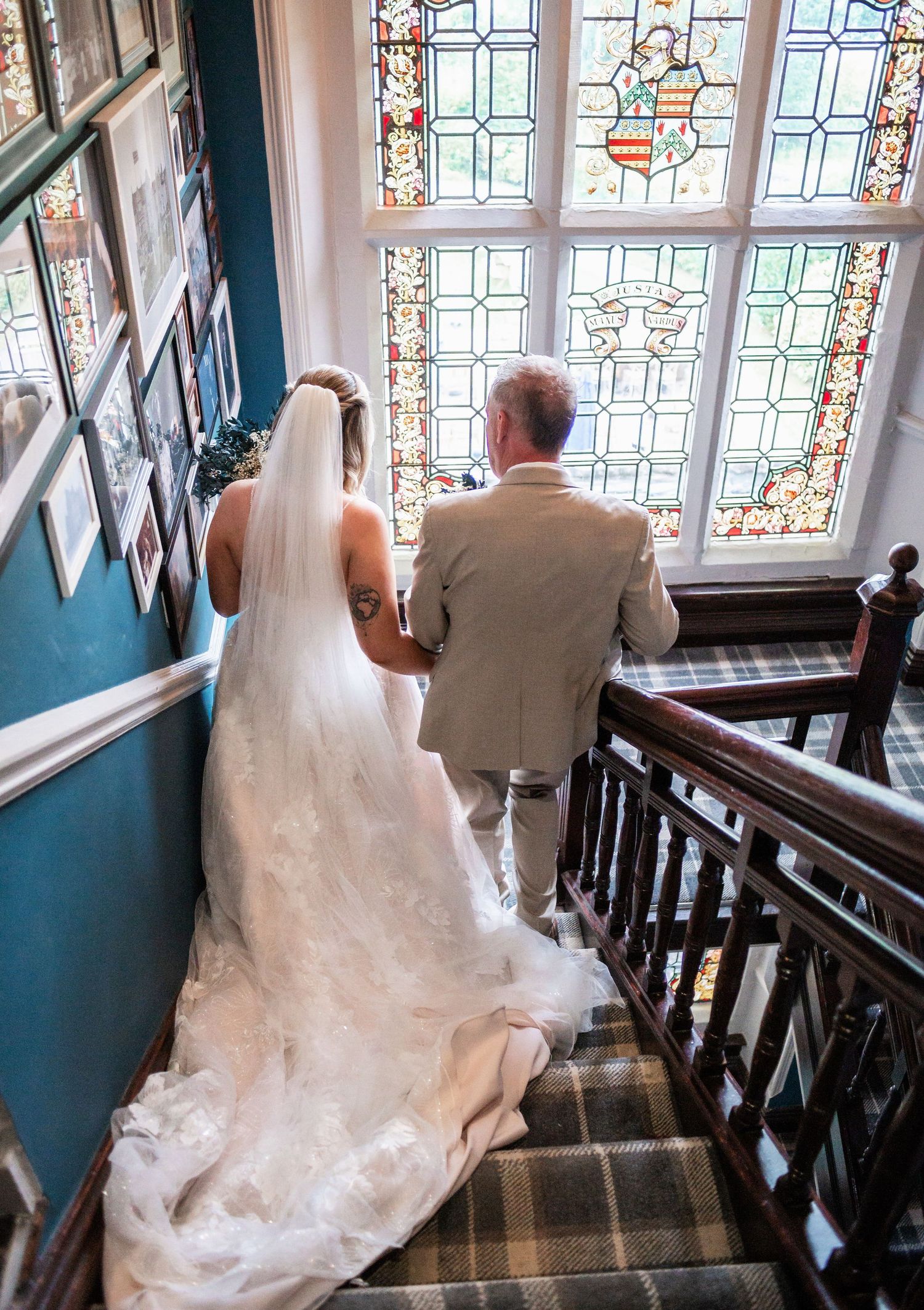 Bride and companion ascending staircase with beautiful stained glass windows in background.