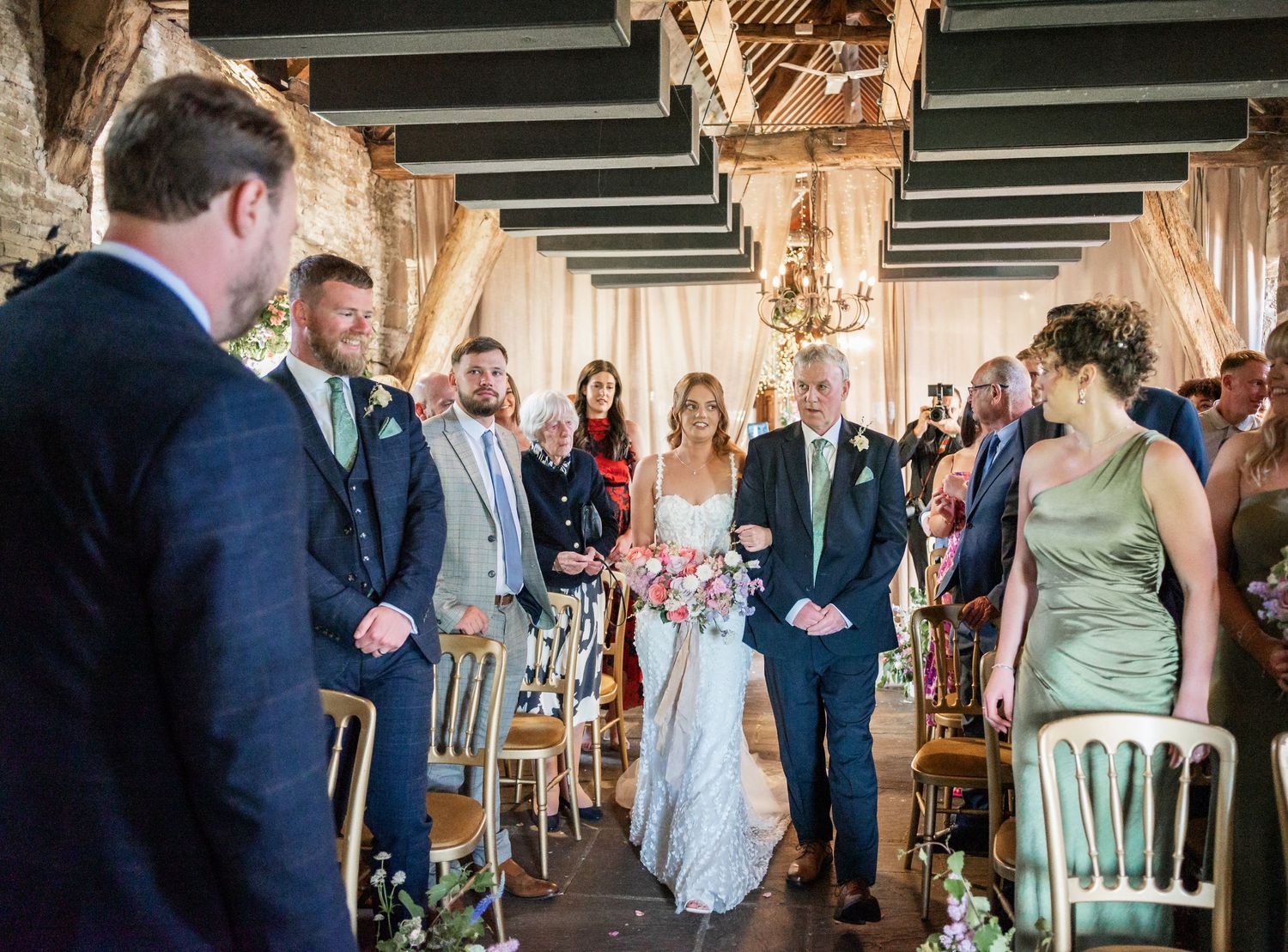 A wedding ceremony takes place in an elegant venue with rustic wooden beams and white decorative chairs.