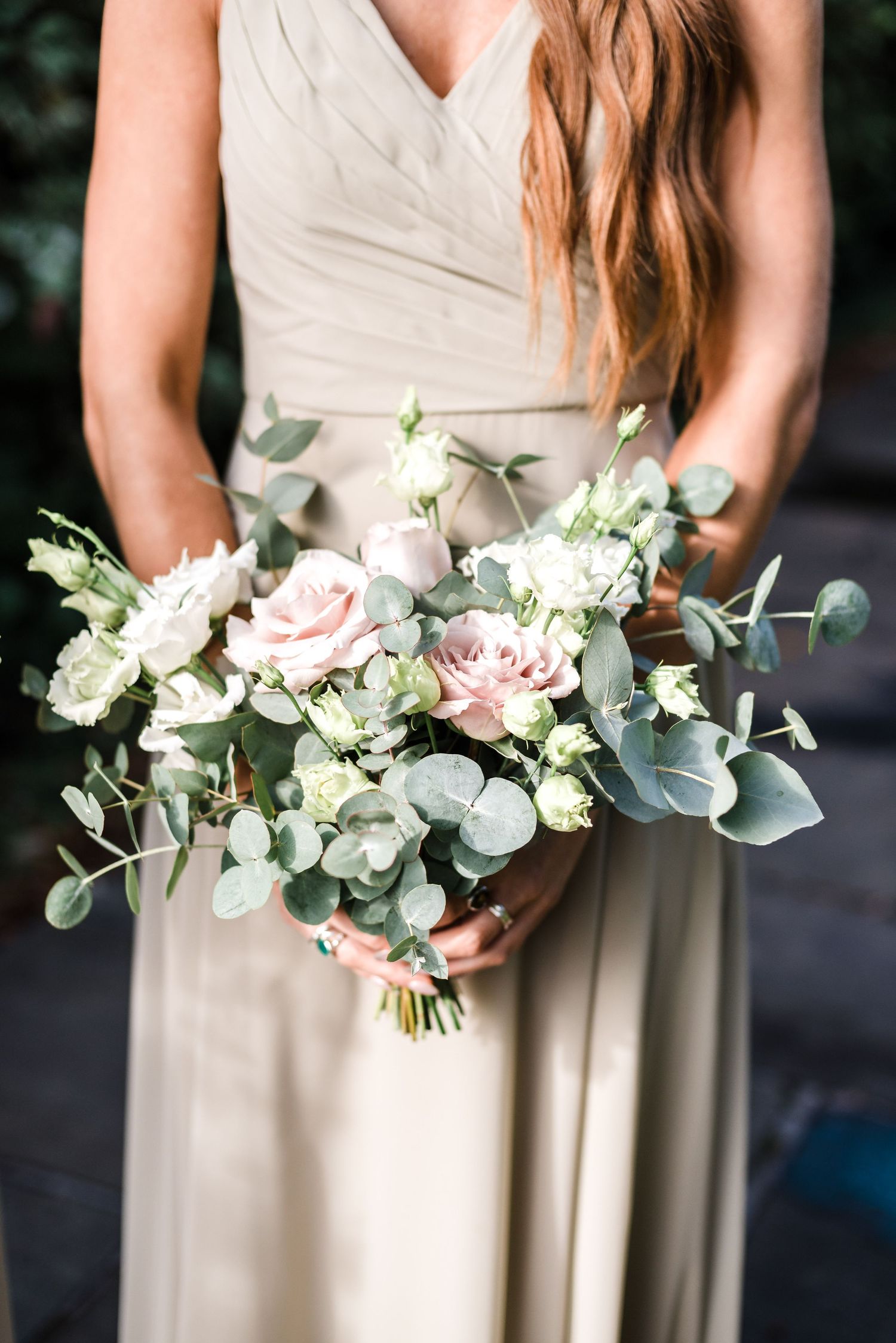 Elegant bridal bouquet with pink roses, white flowers, and eucalyptus held against a light-colored dress.