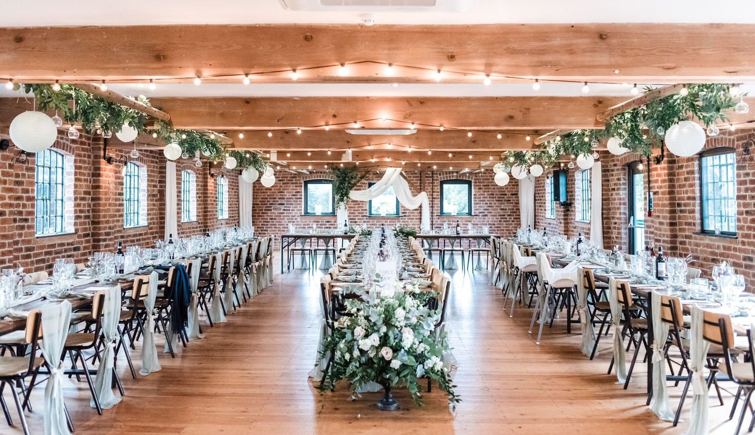 Rustic wedding reception venue with exposed brick walls, wooden beams, and elegant table settings.