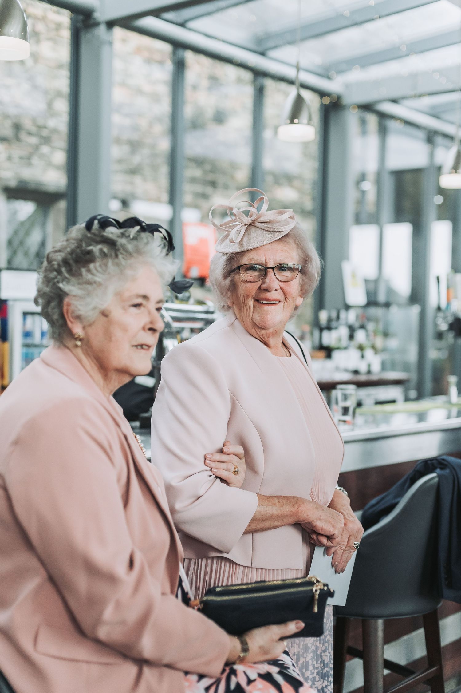 Two ladies in pink outfits share a joyful moment at an elegant venue.