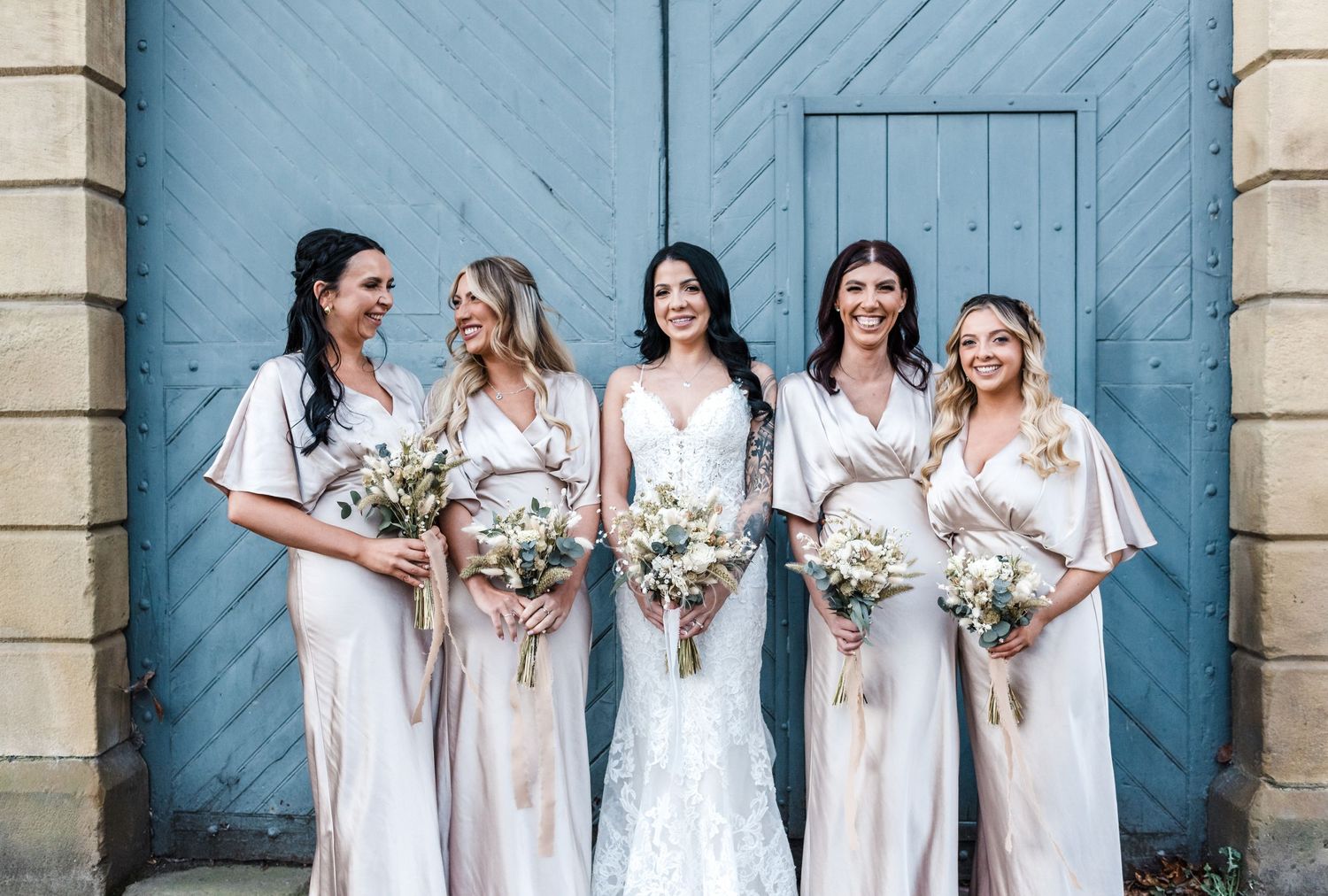 Bridal party in white dresses pose with bouquets against a blue door.