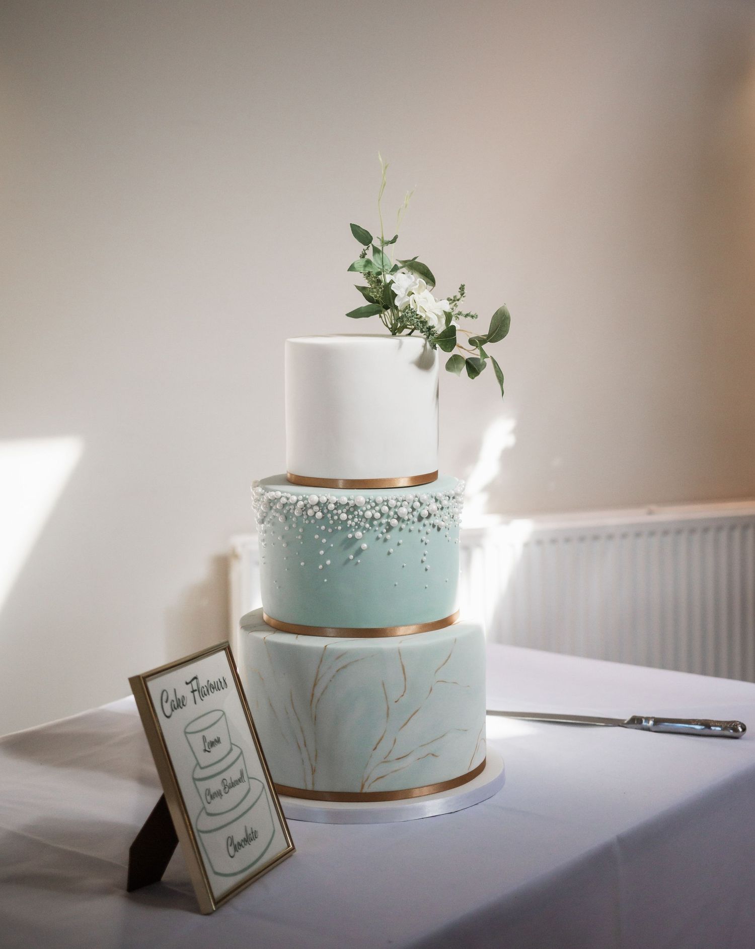 Three-tier wedding cake in white and mint with metallic accents and delicate floral decoration.