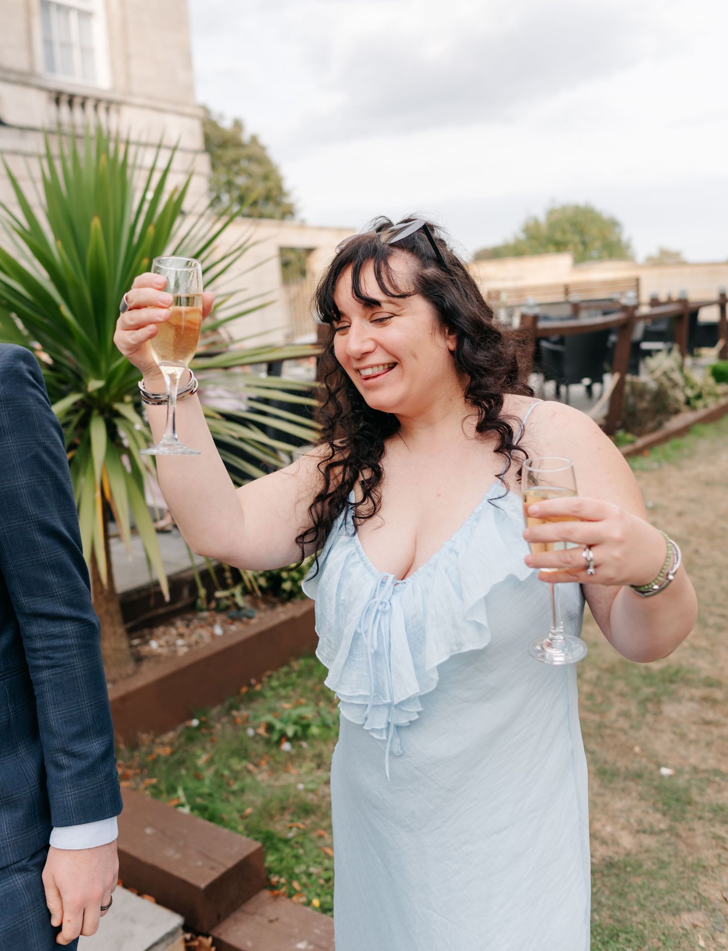Guest in light blue dress raises champagne glass during outdoor celebration.