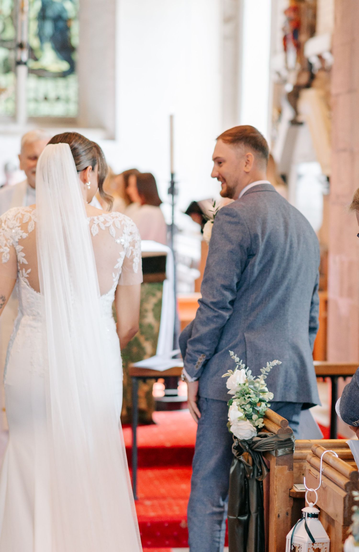 Wedding ceremony inside a church with elegant white decor and red carpet aisle.
