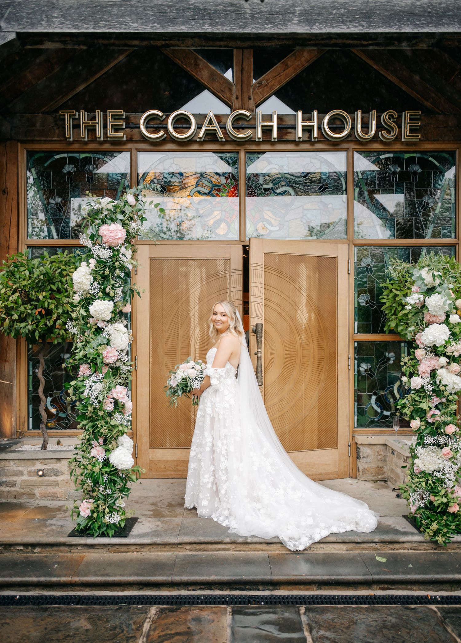 Wedding photos taken outside The Coach House venue with floral decorations and wooden doors.