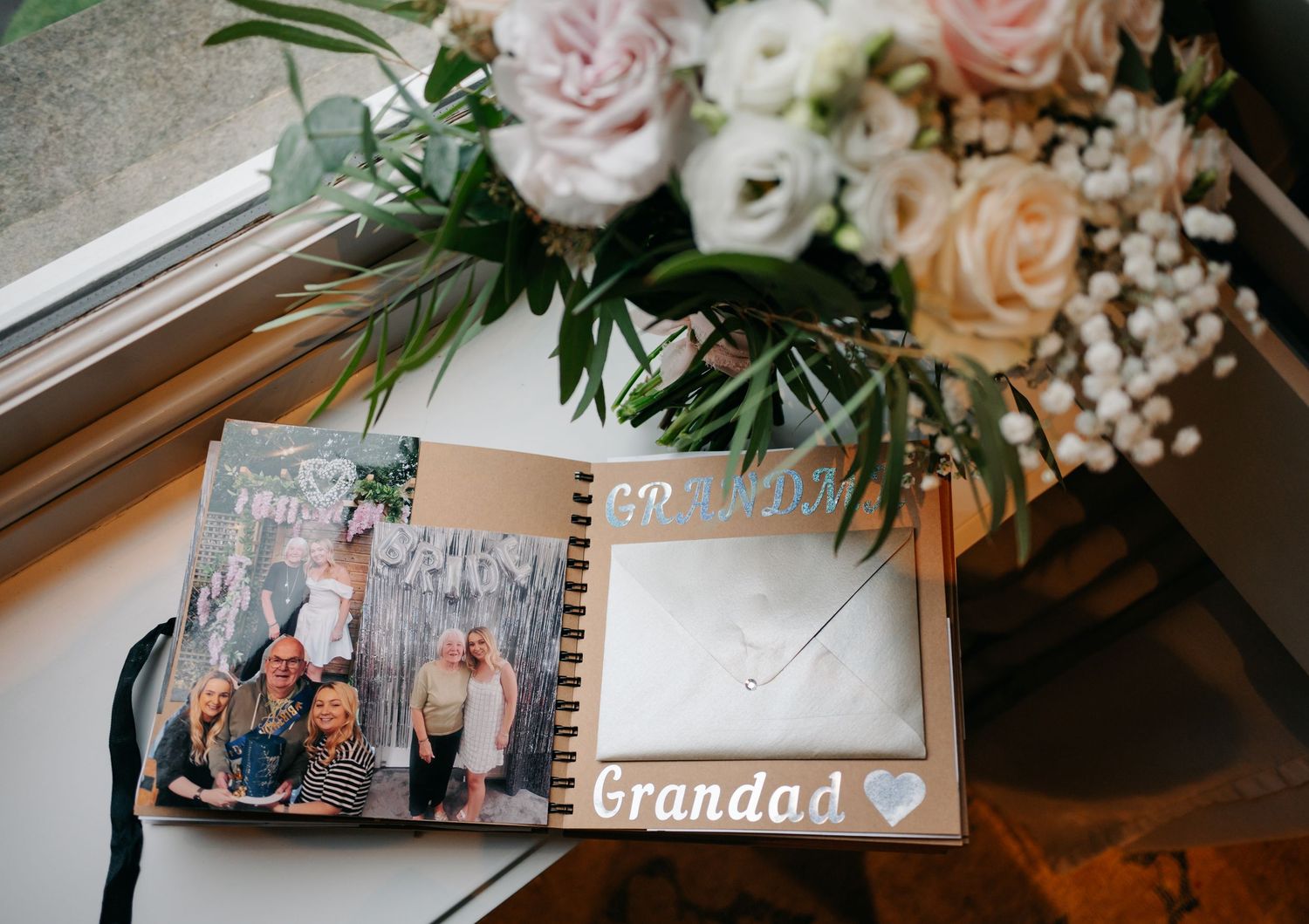 Photo album labeled 'Grandad' with roses and baby's breath floral arrangement on a table.
