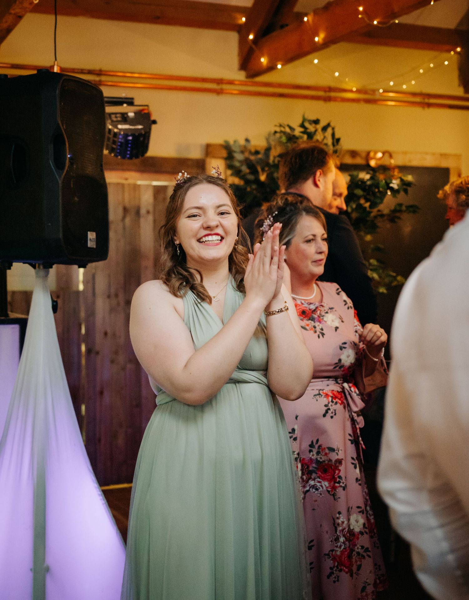 Wedding guests in sage green dresses laughing and clapping during reception celebration.