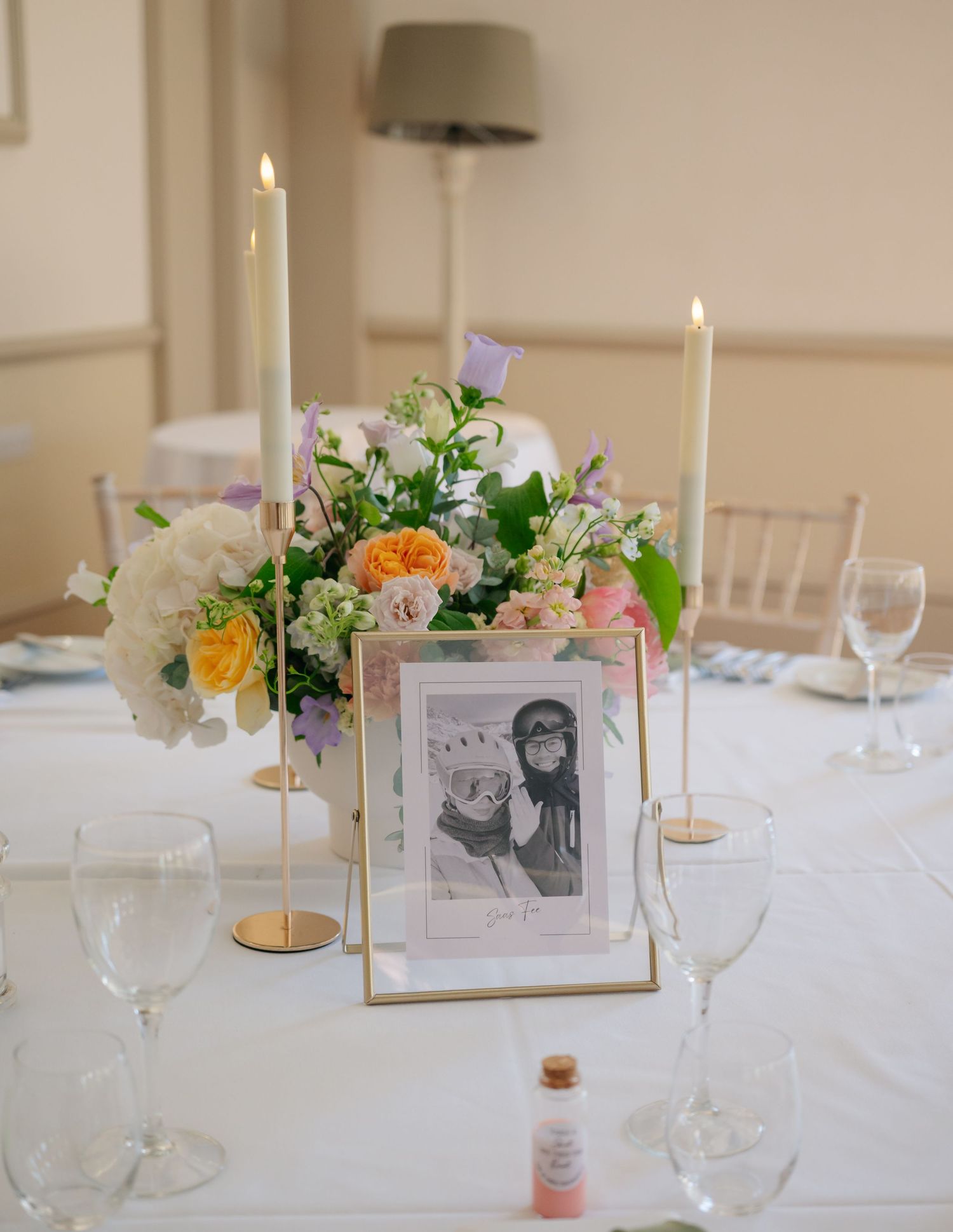 Elegant wedding table setting with white linens, floral centerpieces, candles and framed photos.