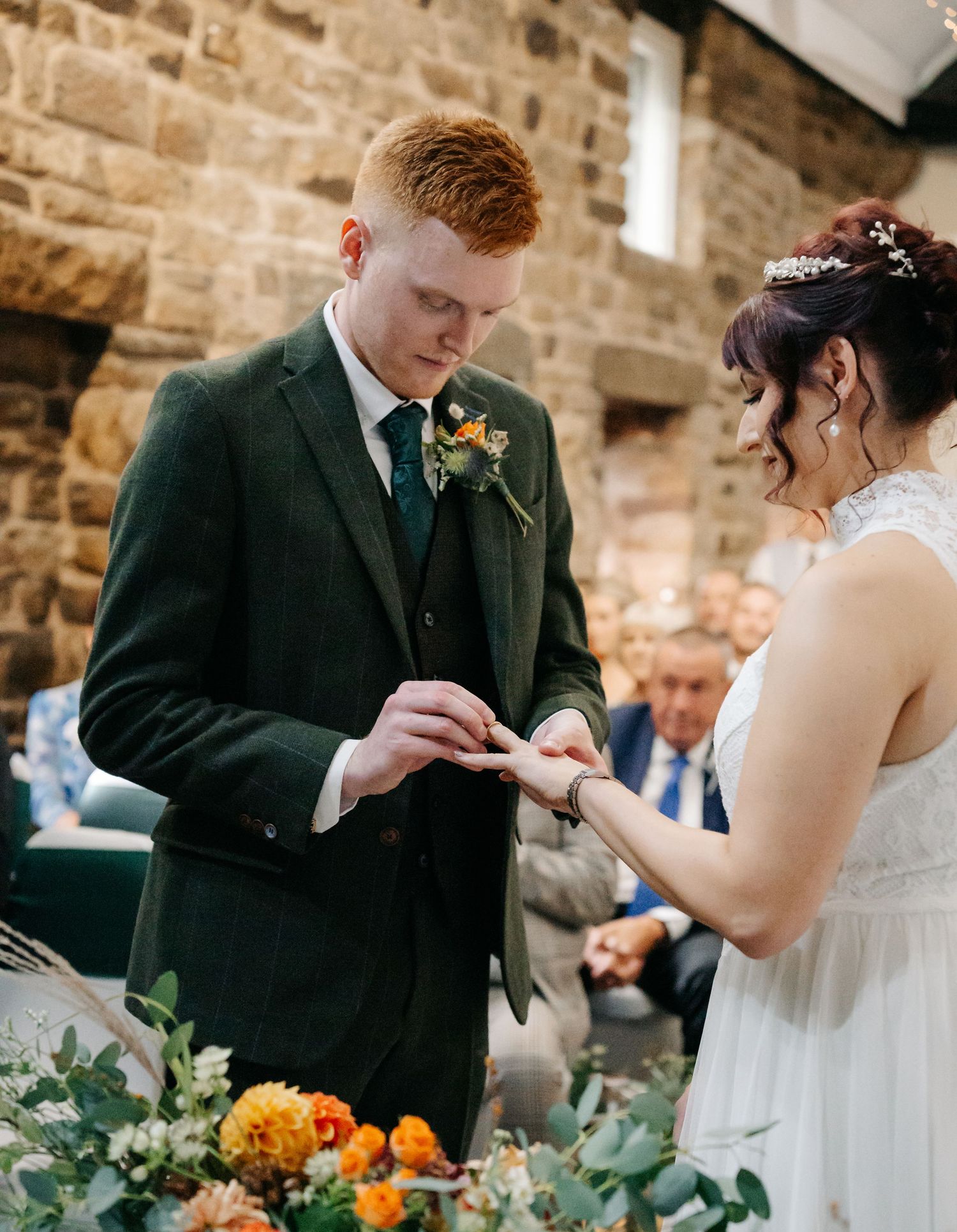 Ring exchange ceremony at rustic stone venue with autumn floral decorations.