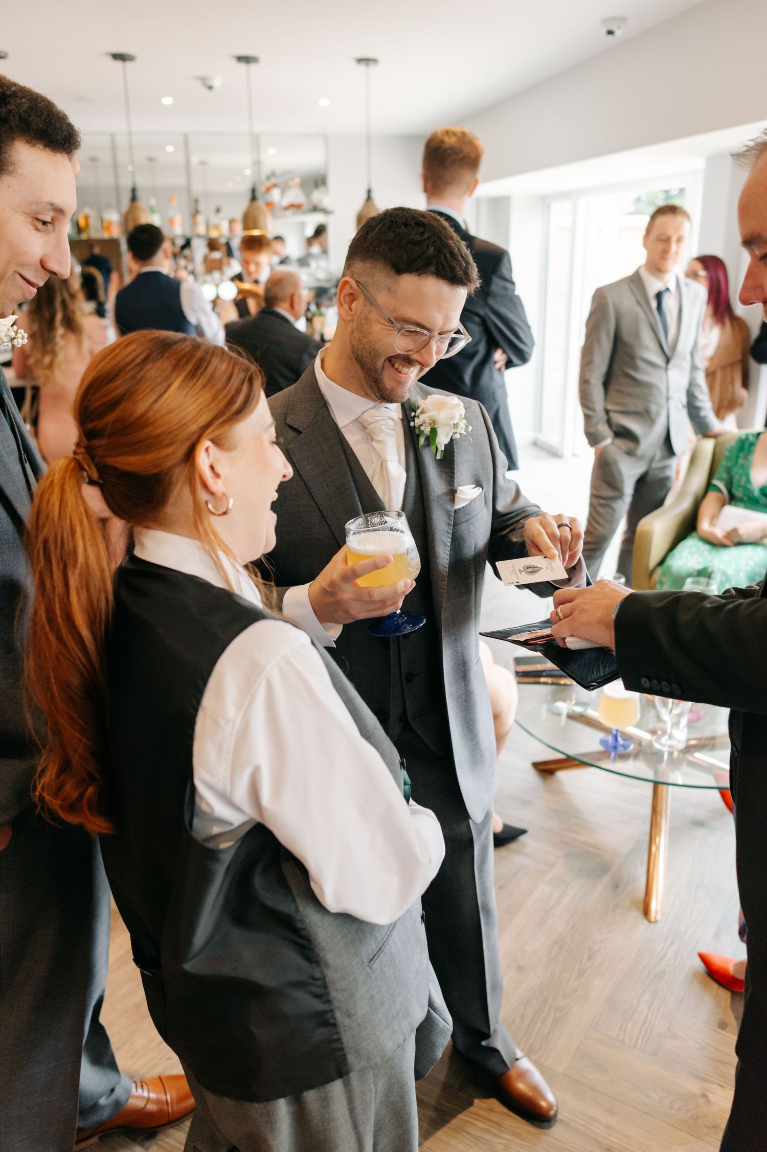 Wedding reception guests mingling and enjoying drinks in a bright modern venue with large windows.