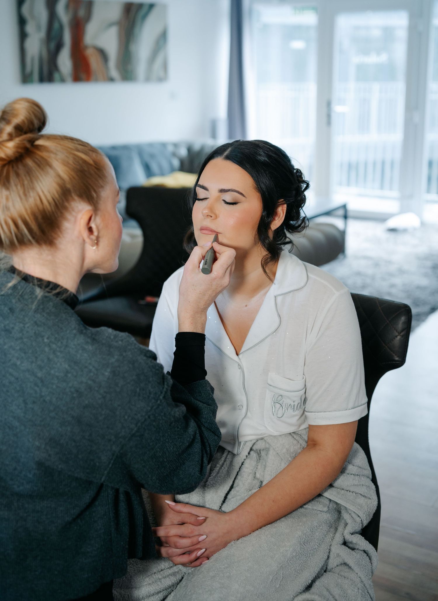 Professional makeup artist applying cosmetics to a client in a white blouse during a wedding preparation session.