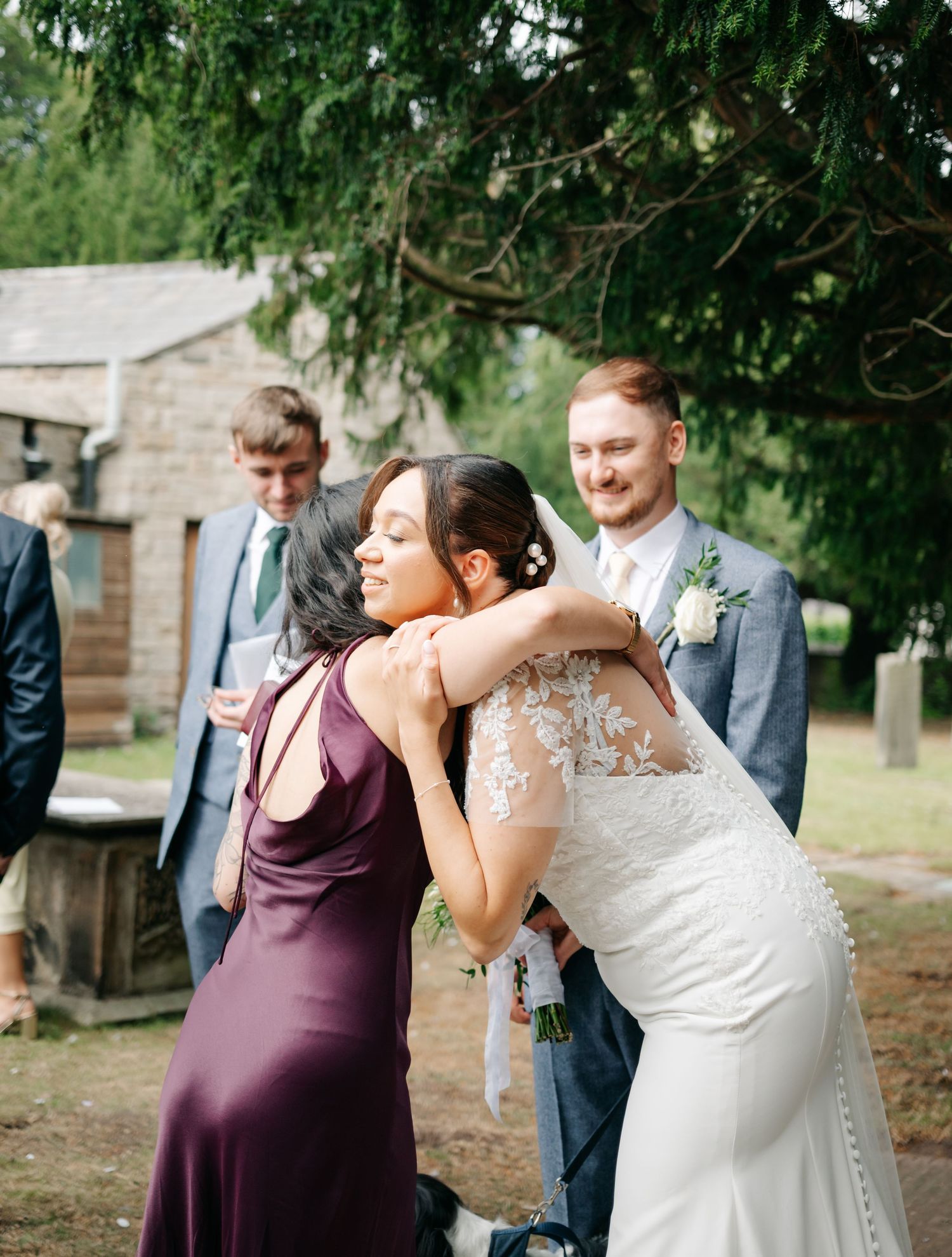 Wedding party members share emotional embraces during outdoor celebration.