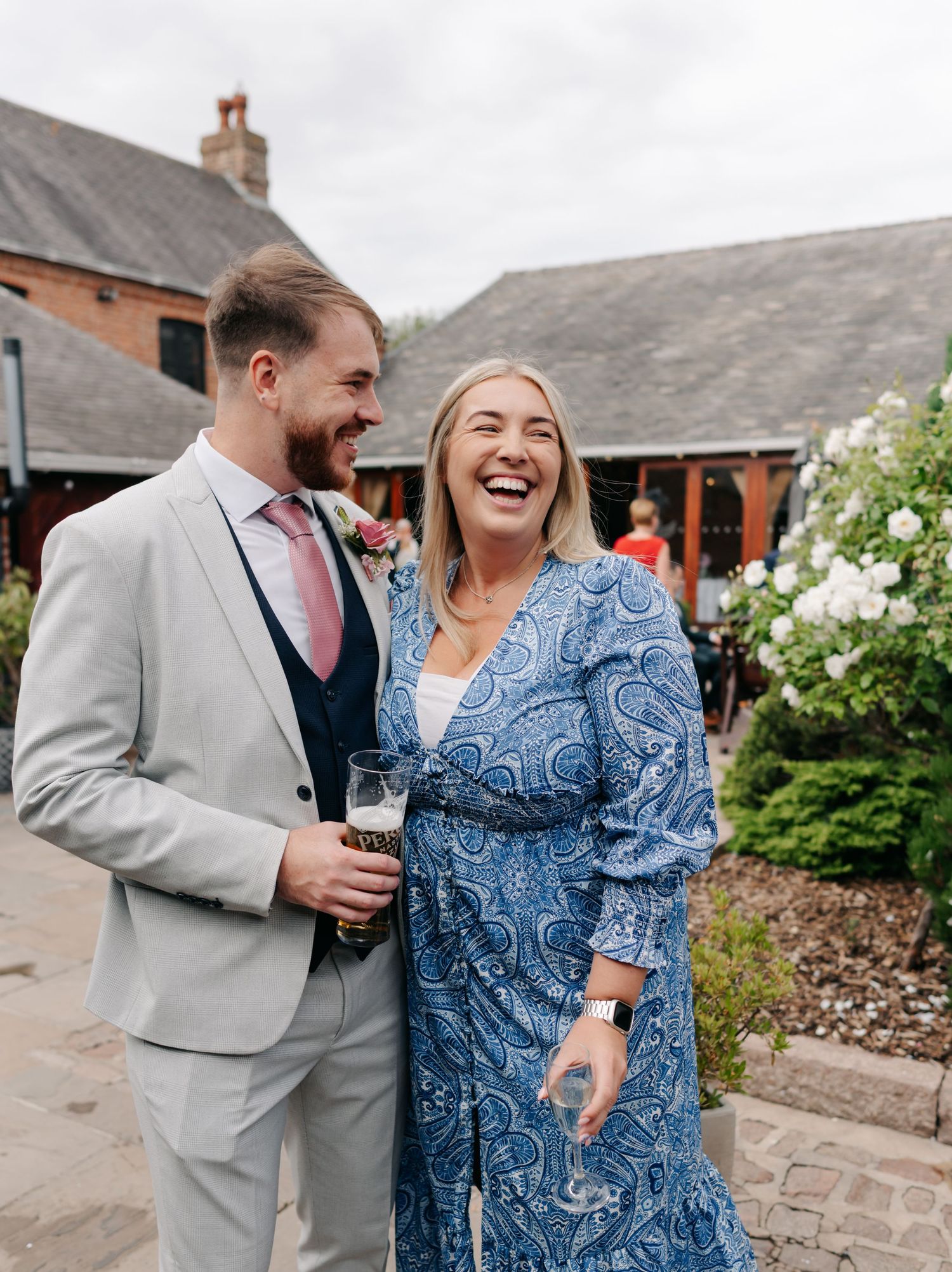 Wedding guests in formal attire sharing laughter and drinks at an outdoor reception venue.