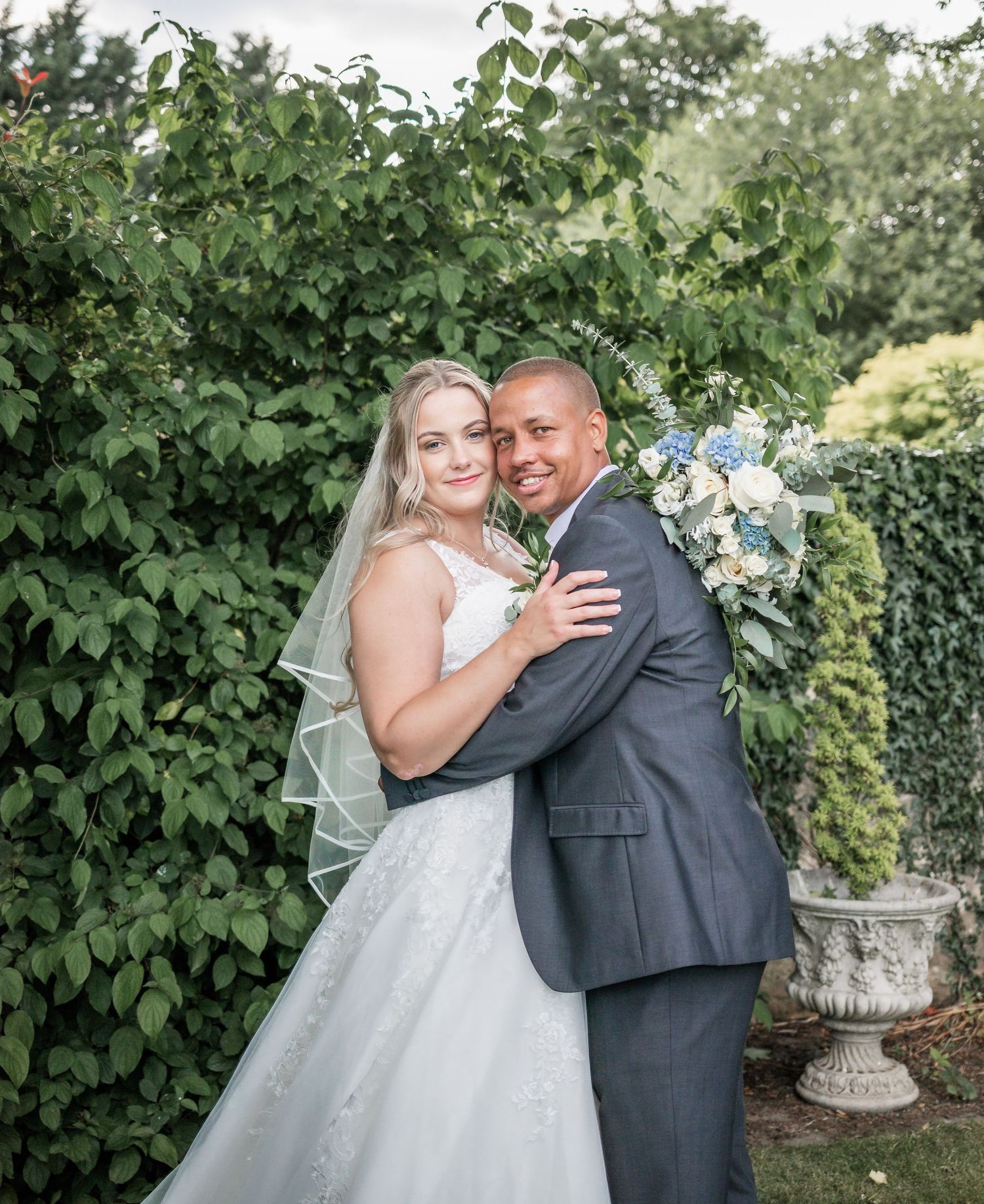 Garden wedding portrait with lush greenery and blue floral bouquet.