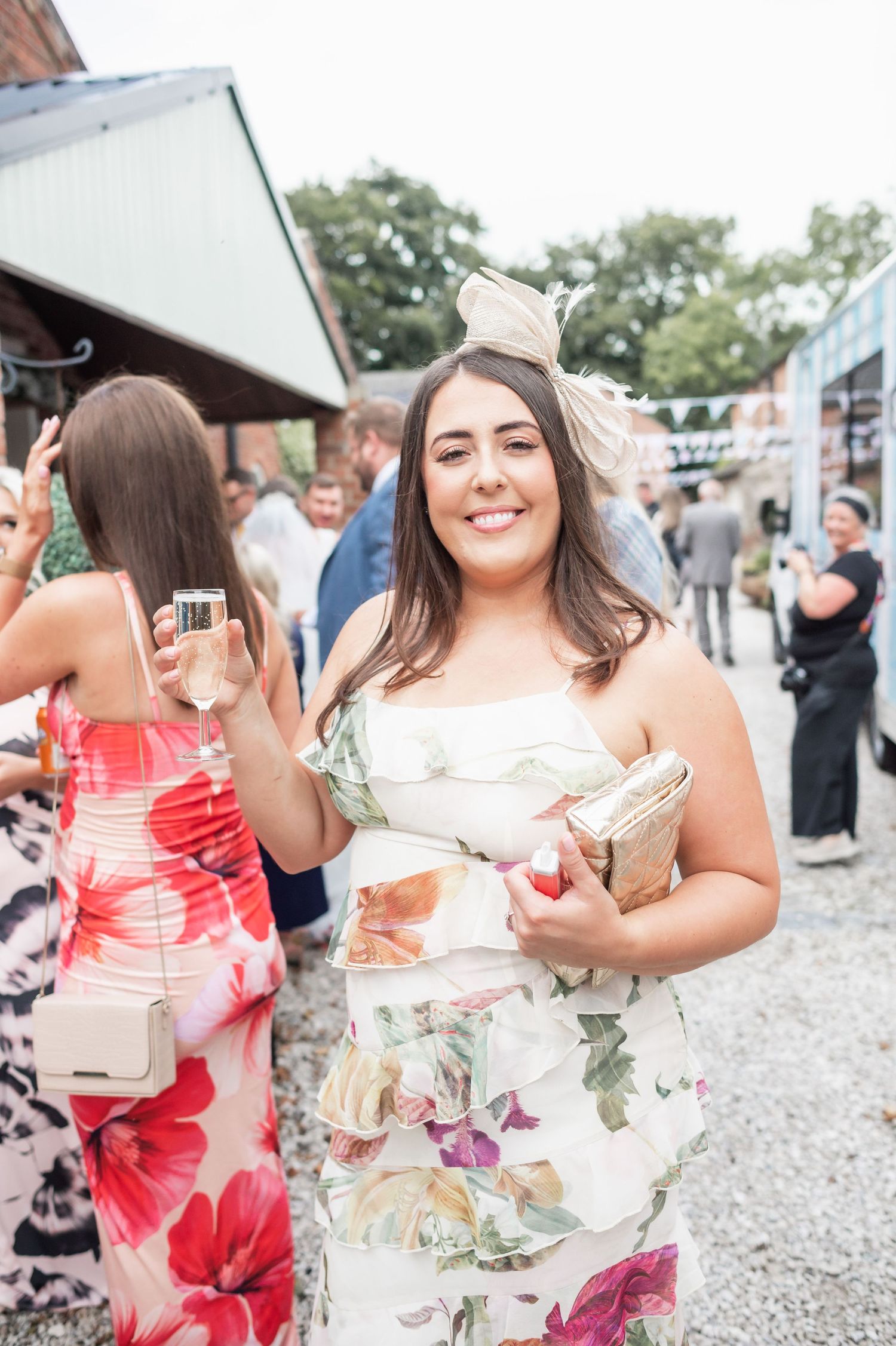 A wedding guest in a floral dress holds a champagne glass at an outdoor reception.