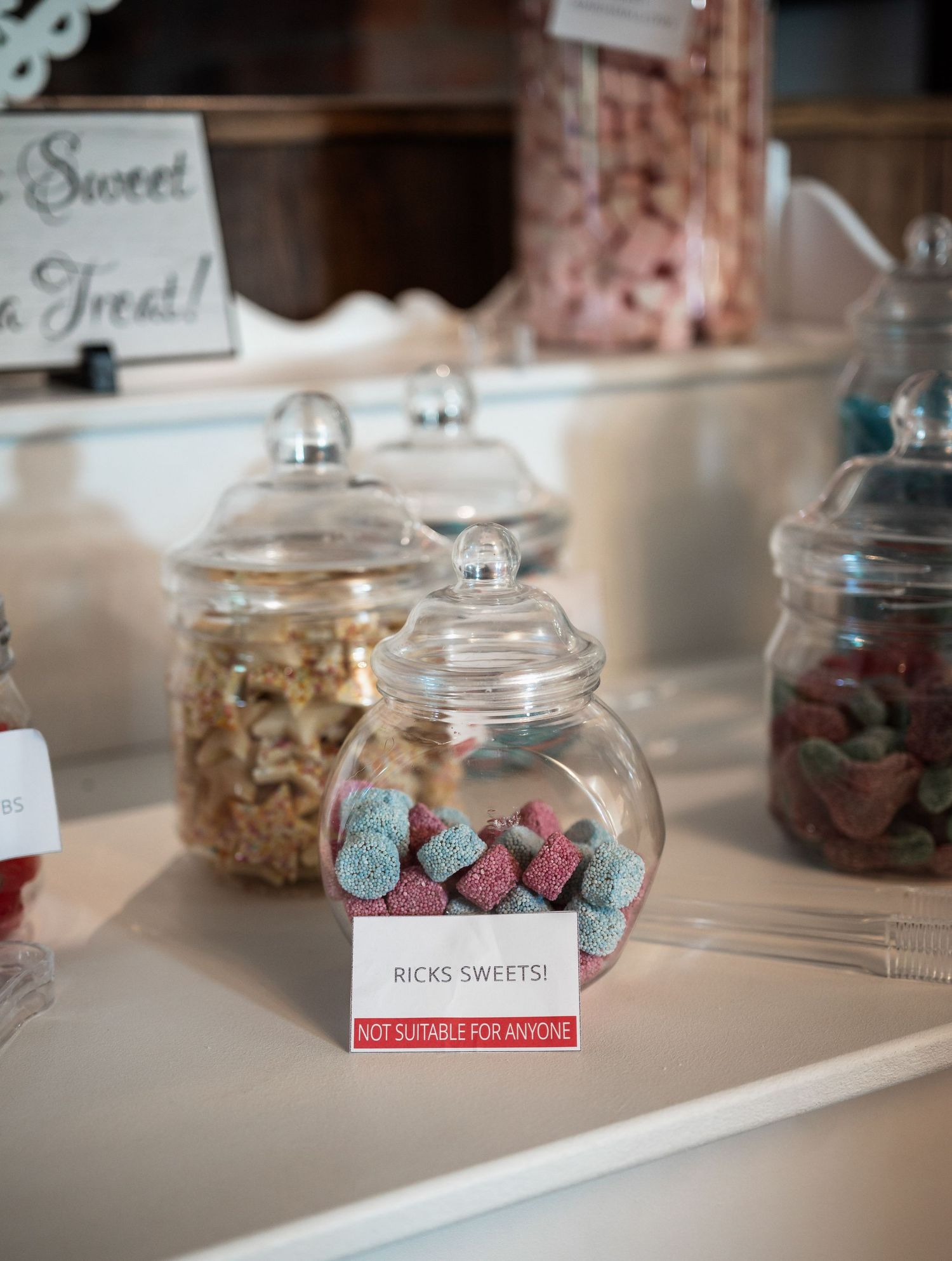 Glass candy jars filled with colorful sweets at wedding dessert table.