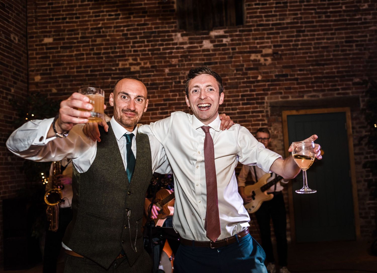 Two celebratory guests raise their glasses while dancing at a wedding reception.
