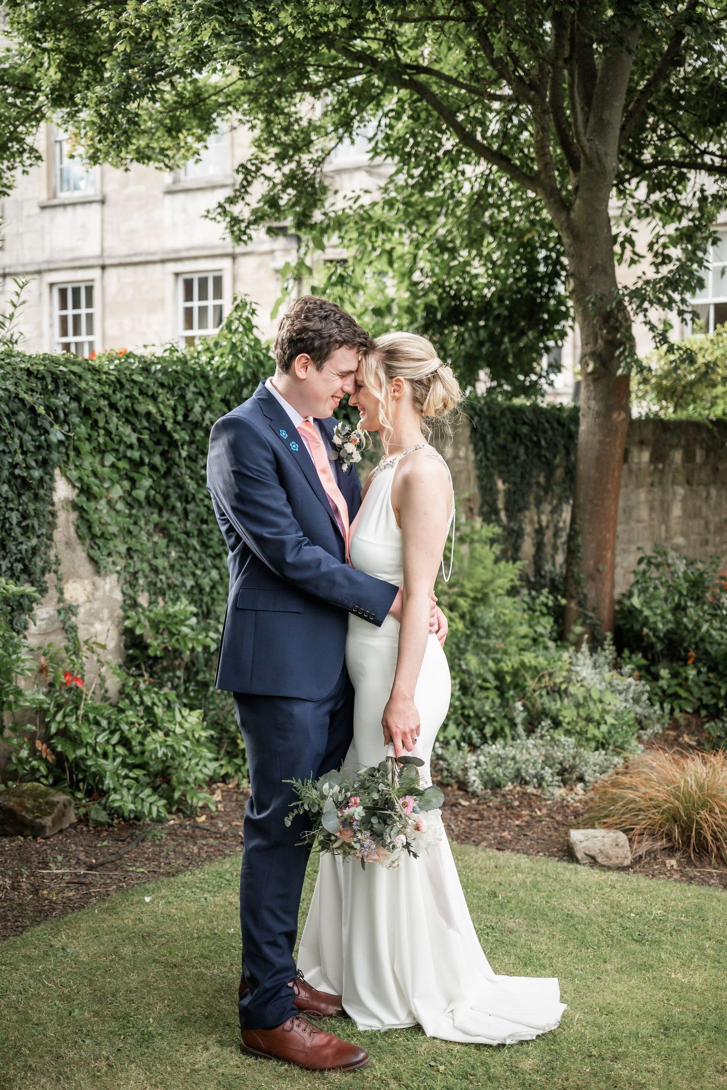 A romantic wedding portrait captured in a garden with an ivy-covered wall backdrop.