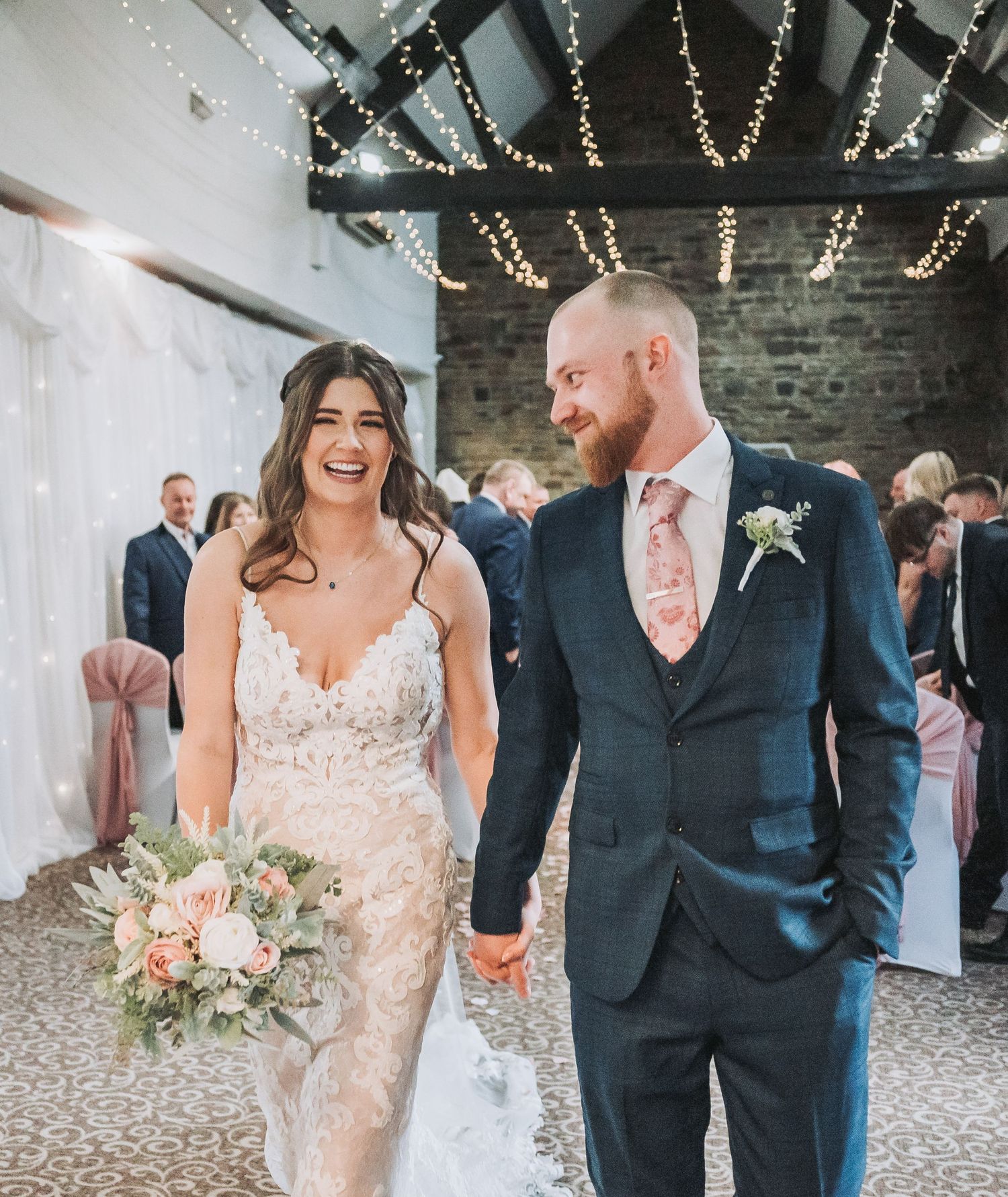 Wedding couple laughing together under string lights in rustic brick venue.
