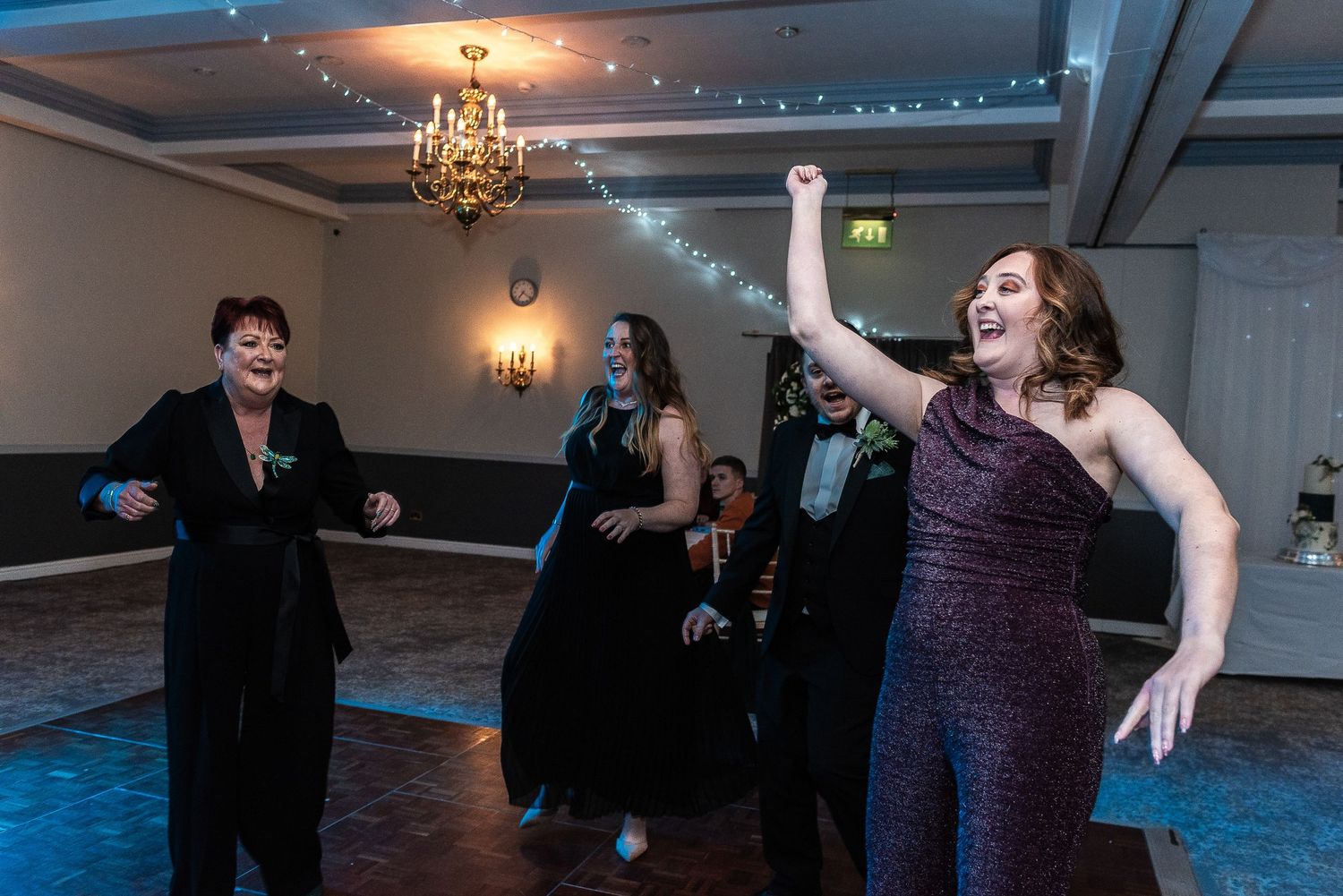 Wedding guests dancing and celebrating on a lit dance floor during an evening reception.