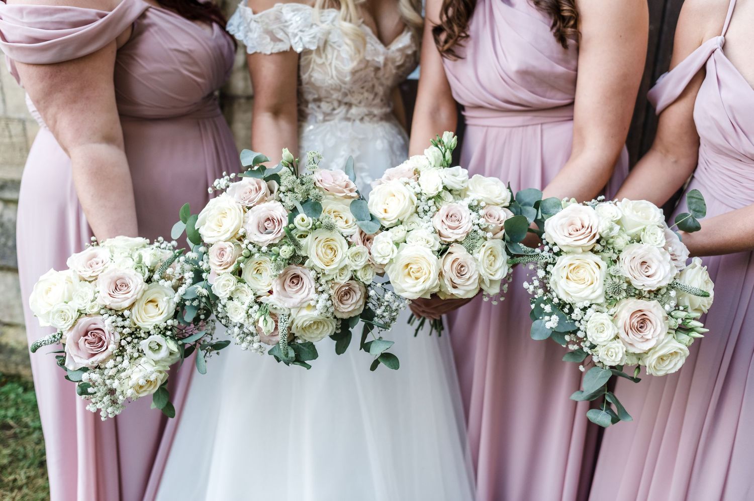 Bridesmaids in pink dresses hold matching white and blush floral bouquets.