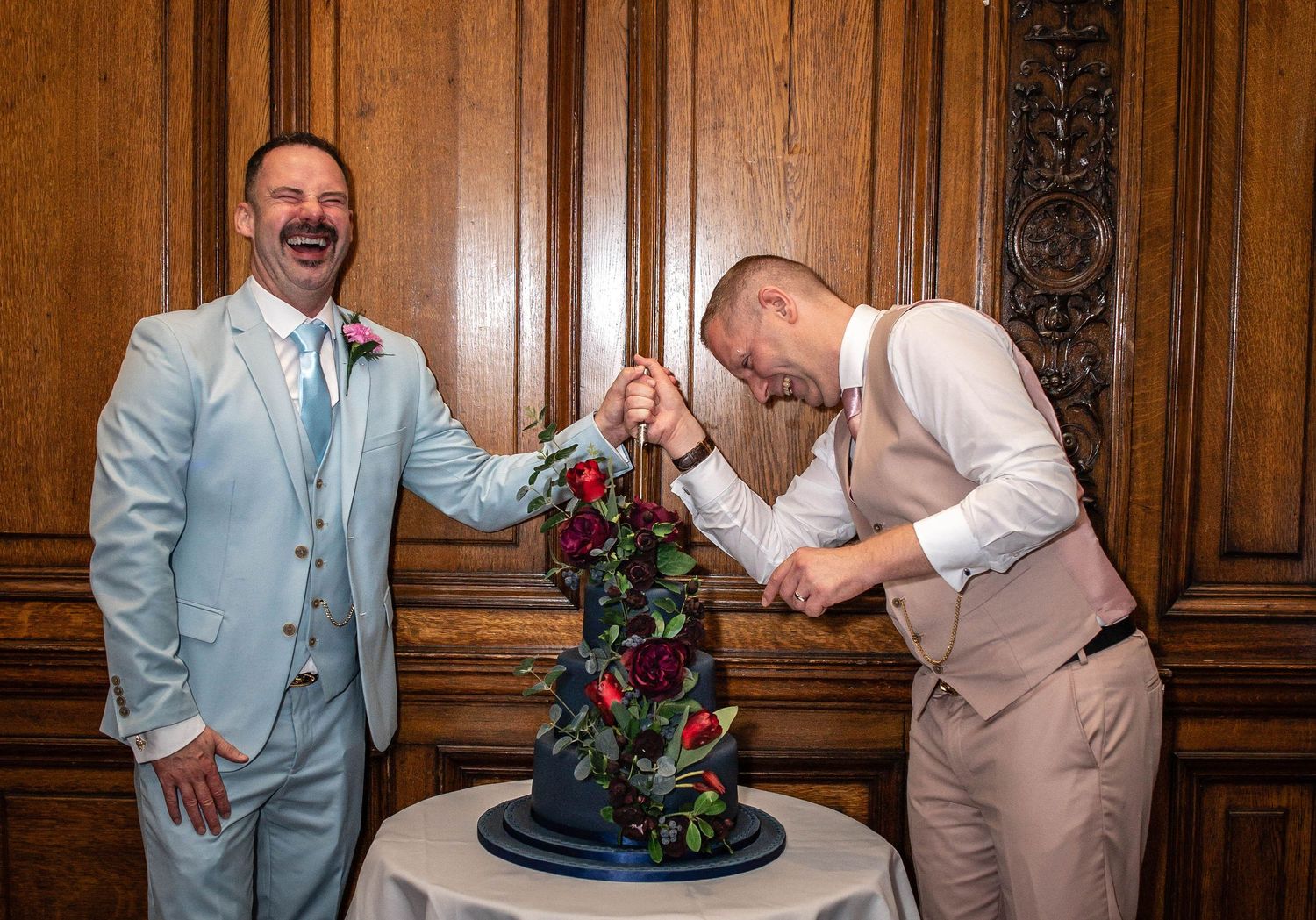 Two people in formal attire pose with a dark blue tiered wedding cake.