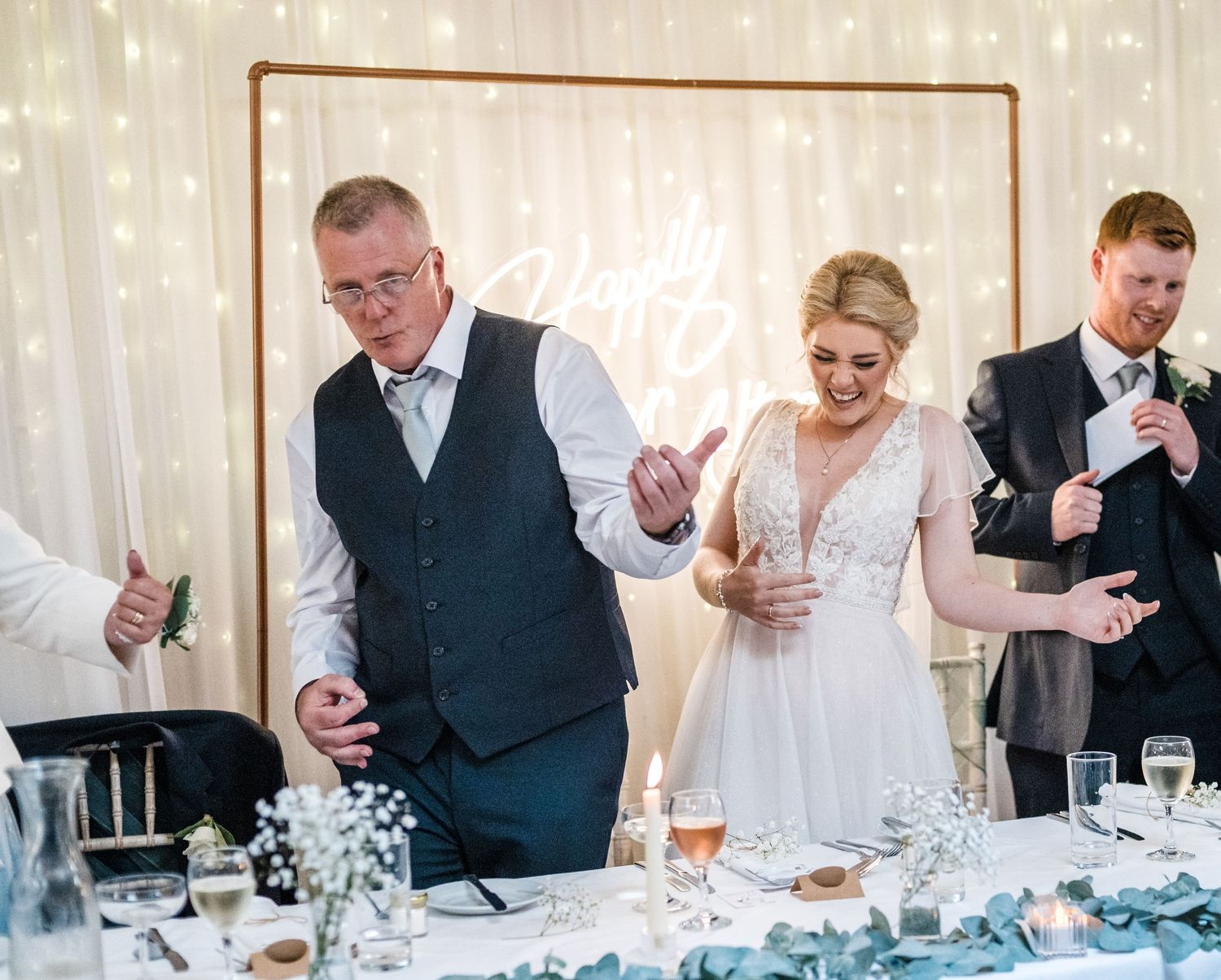Guests celebrate at a wedding reception table decorated with white linens and table settings.