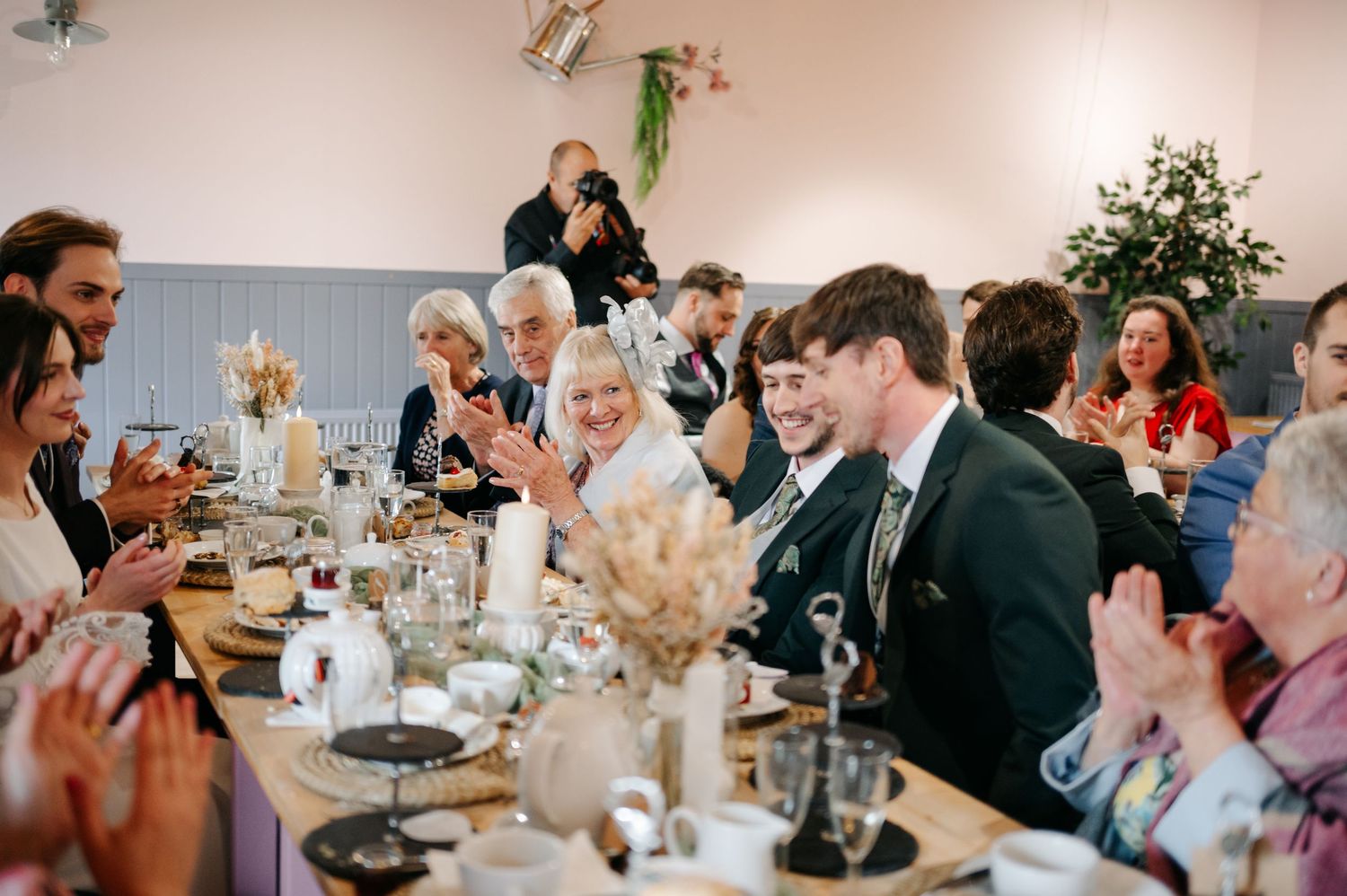 Wedding reception guests seated at decorated tables with warm lighting and floral centerpieces.
