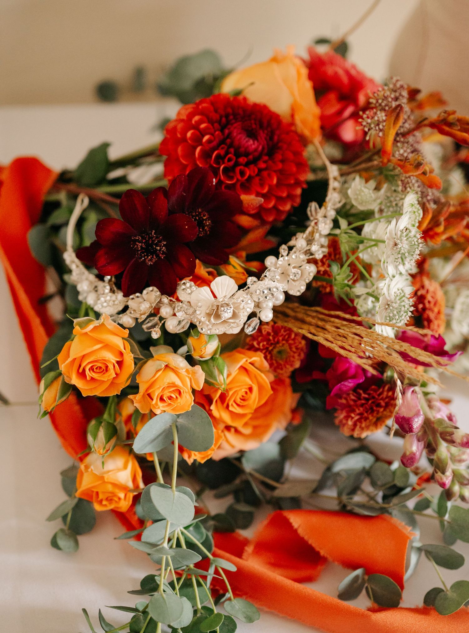 Vibrant floral arrangement featuring orange roses, deep red dahlias, and eucalyptus greenery.