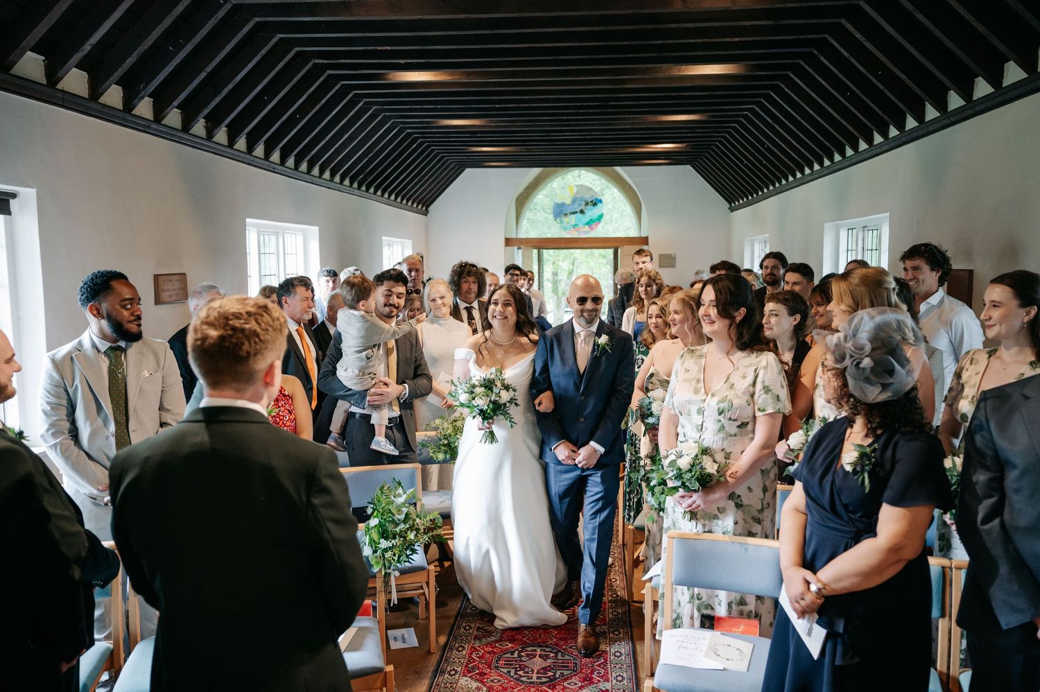 Wedding guests mingle and celebrate in an elegant reception hall with white walls and natural lighting.