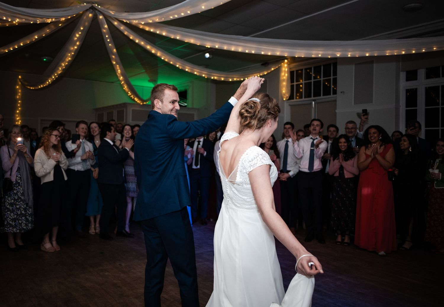 A couple dances under twinkling lights at their wedding reception while guests watch from the sidelines.