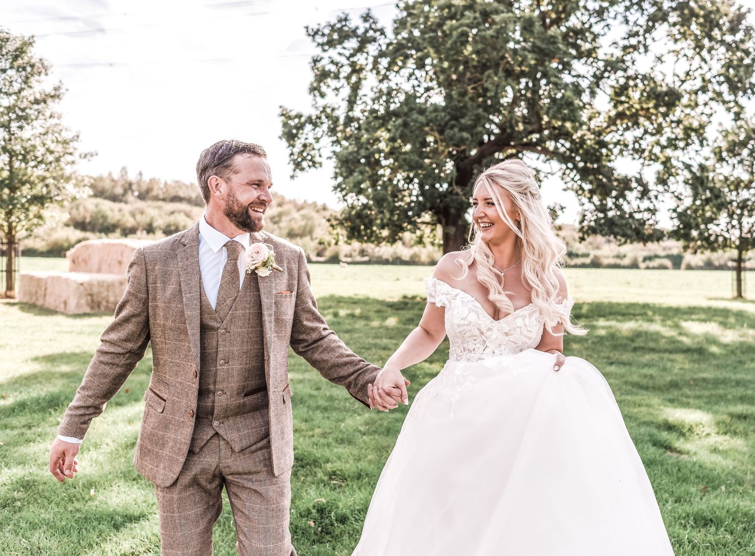 A couple in wedding attire dances joyfully together in a sunny outdoor garden setting.