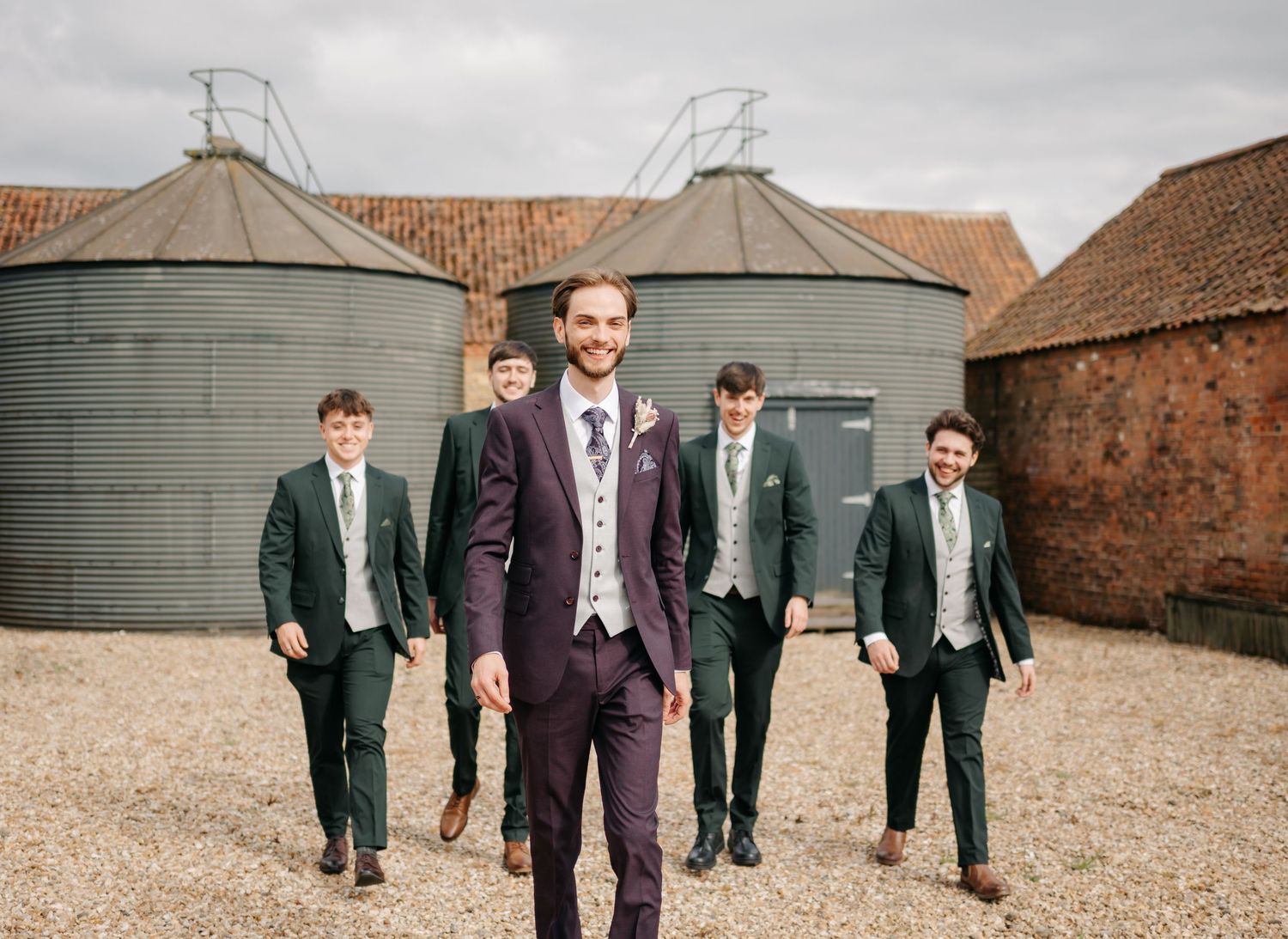Wedding party walking across rustic courtyard with brick buildings.