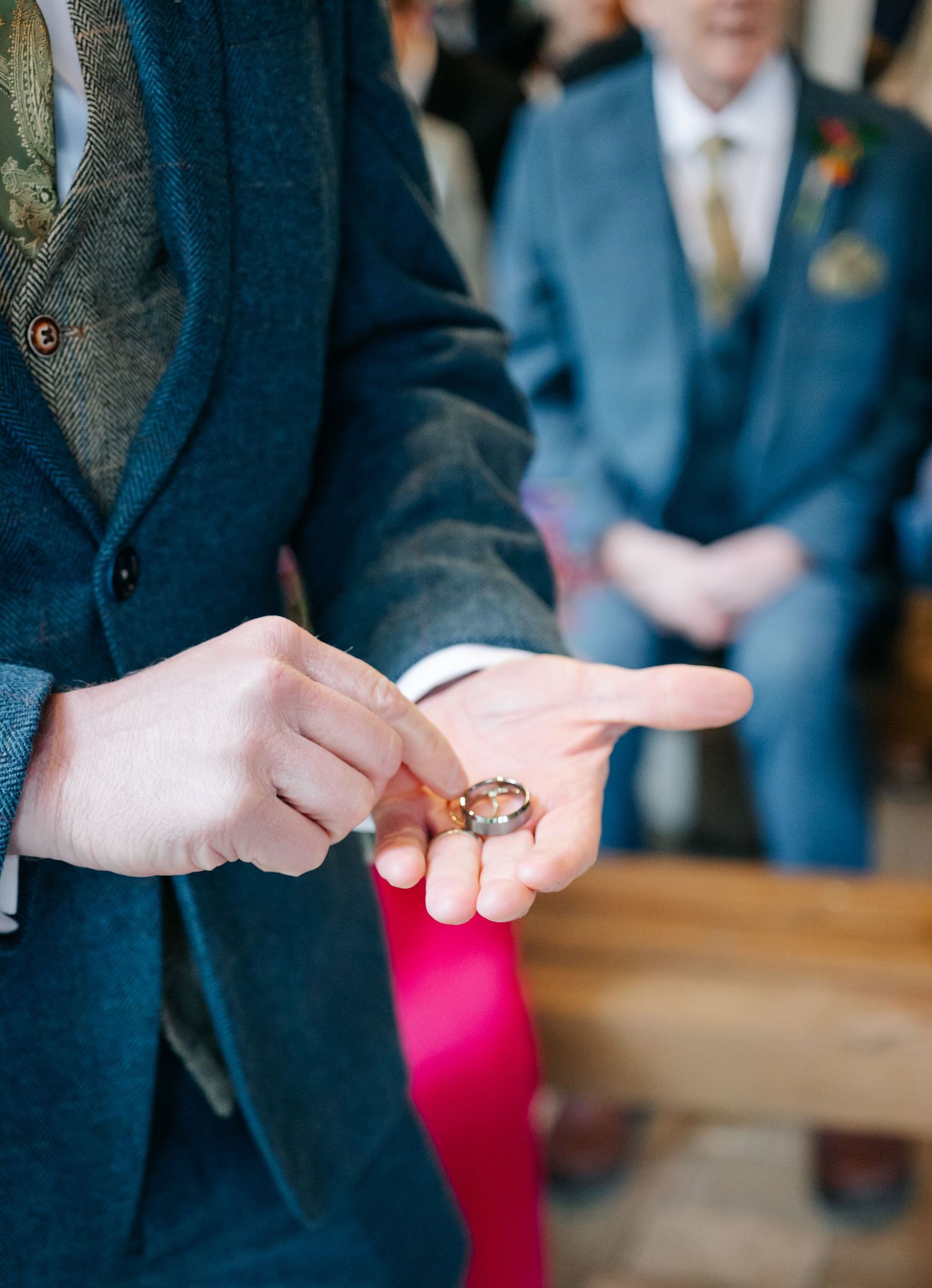 Close-up shot of hands during a ring exchange ceremony with navy suits in the background.