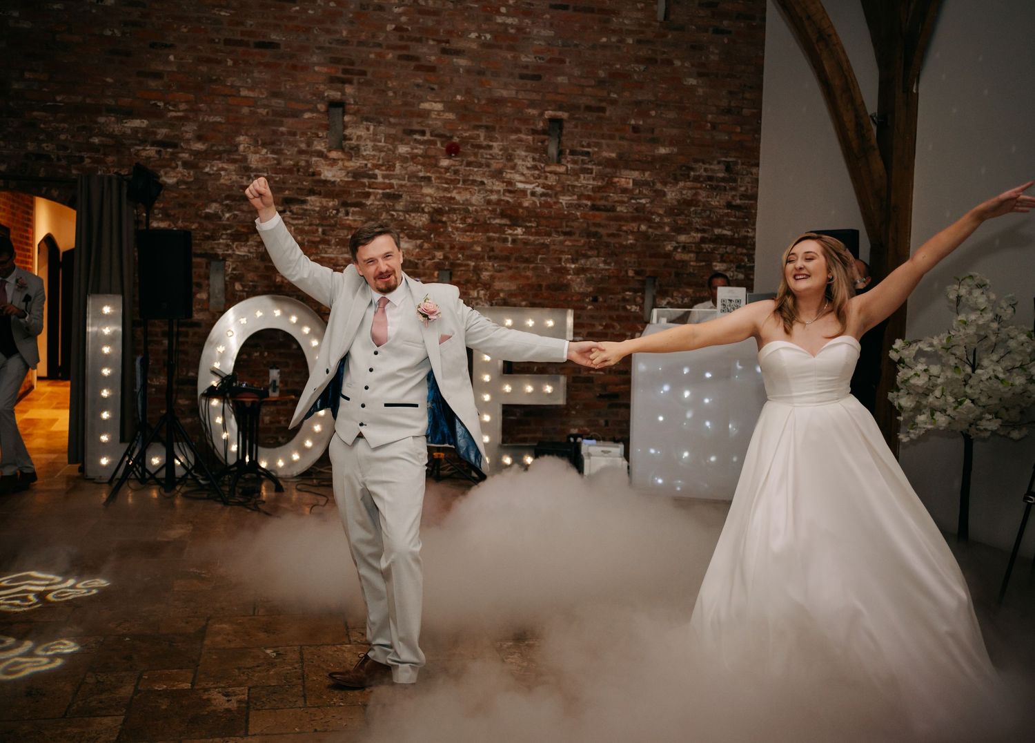 Wedding dance party in full swing against rustic brick walls with dramatic lighting.