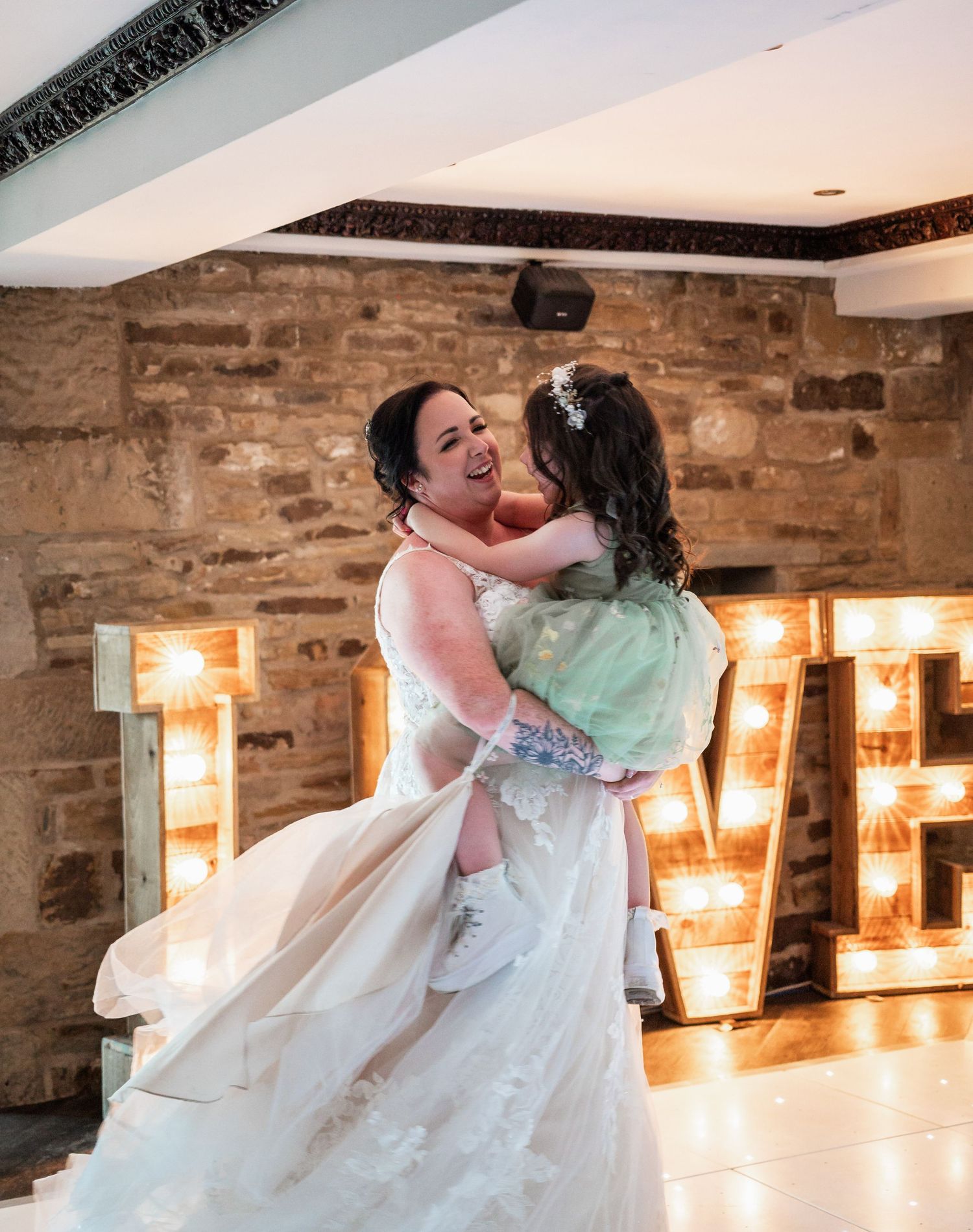 A joyful dance moment in front of illuminated letters at a wedding reception with exposed stone walls.