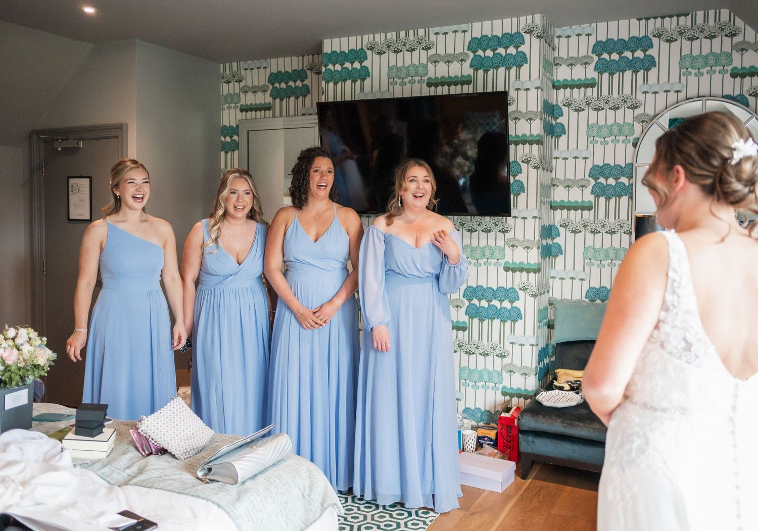 Bridesmaids in powder blue dresses getting ready in a modern room with patterned wallpaper.