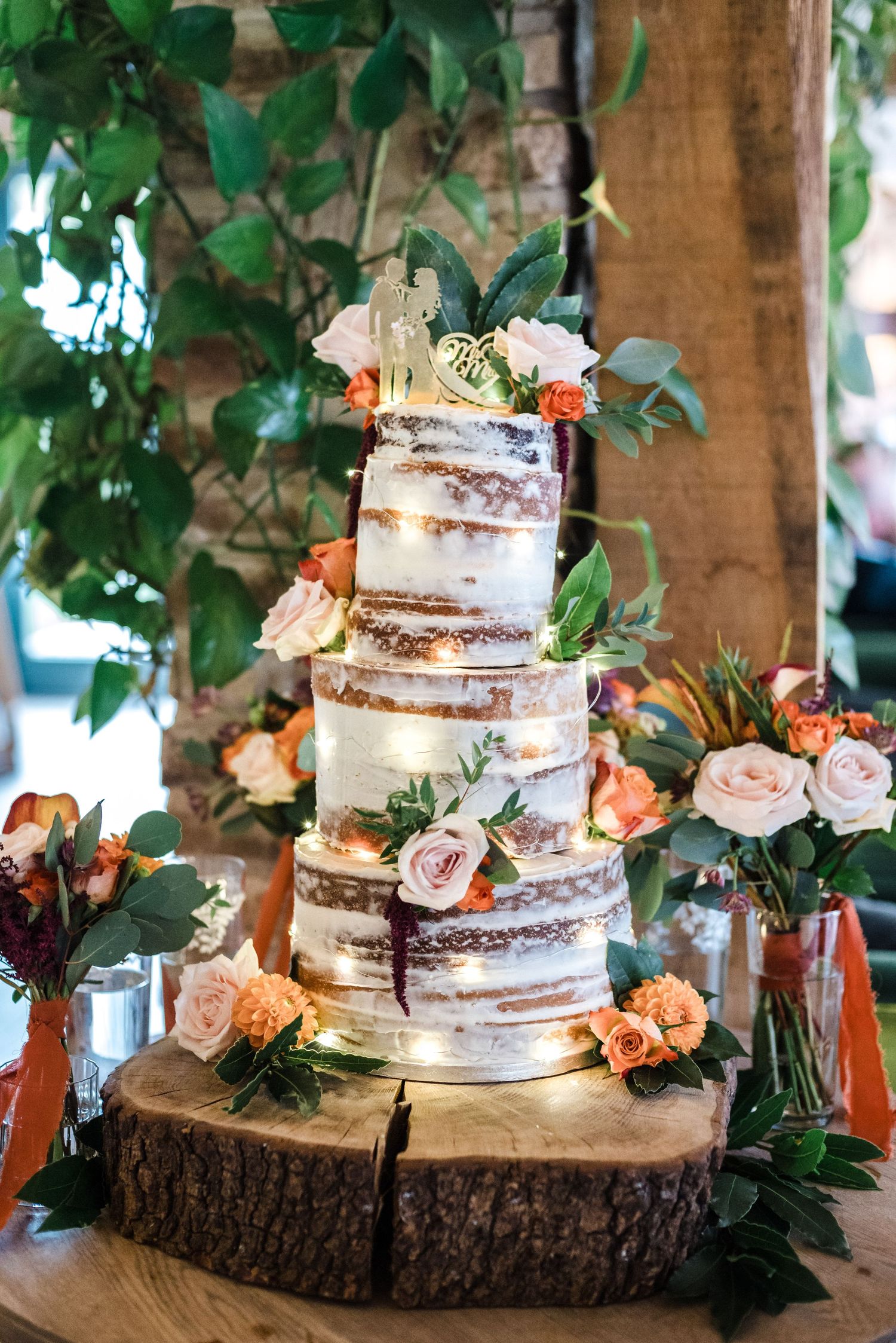 Semi-naked wedding cake decorated with fresh flowers on rustic wood slice base.
