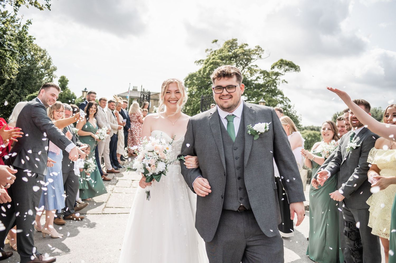 Wedding couple walking through shower of confetti with celebrating guests along pathway.