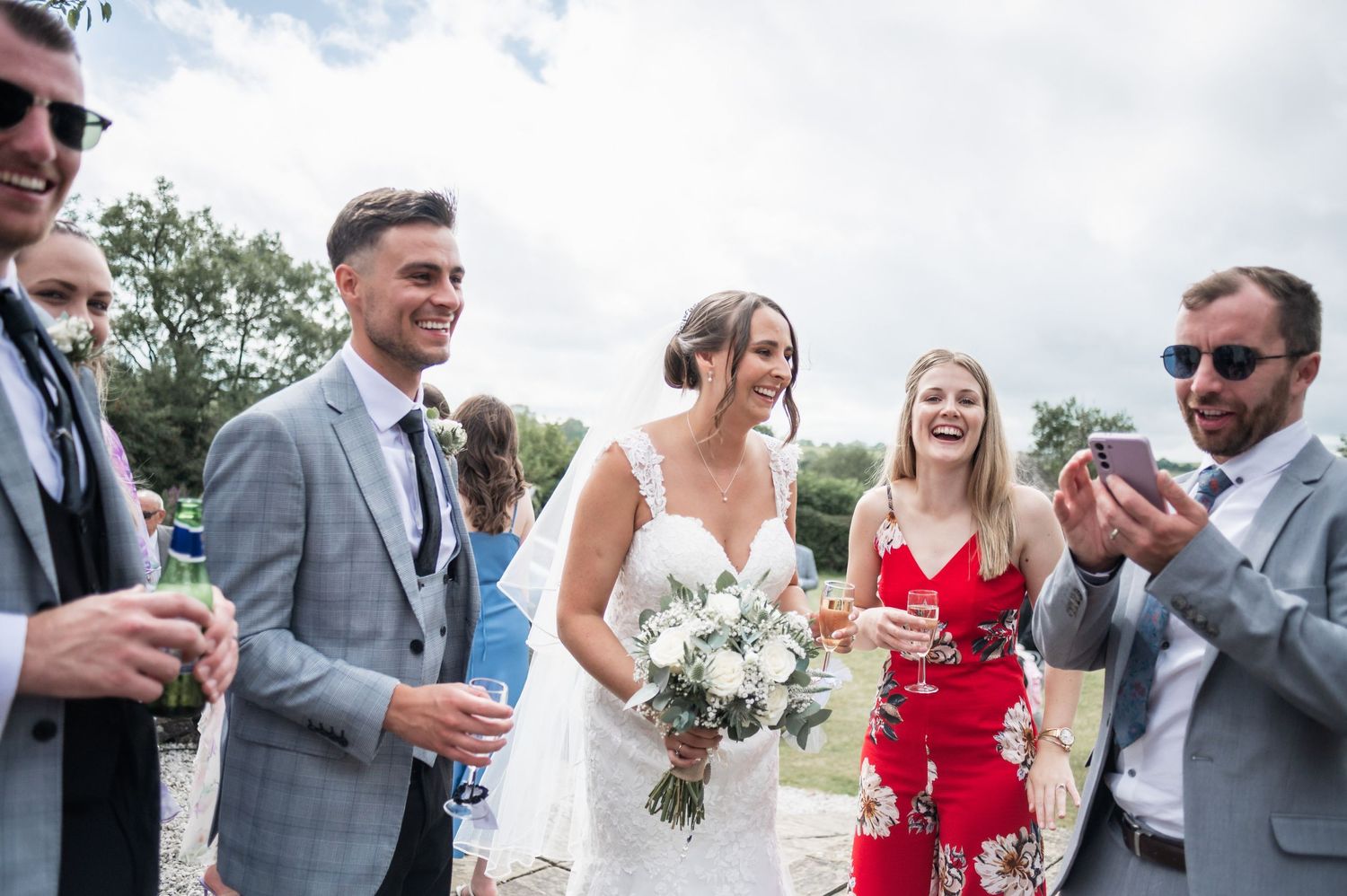 Wedding party members gather outdoors for celebratory drinks and photos.